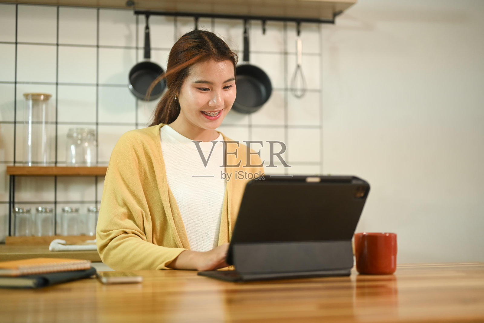 快乐的年轻亚洲女人在厨房柜台前摆弄着电子平板电脑照片摄影图片