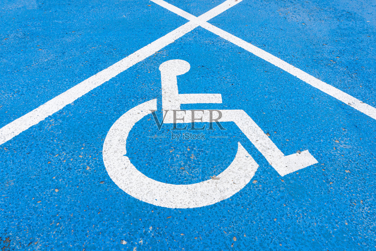 地上有残疾人停车标志。轮椅的象征。白色和蓝色的停车场油漆。三角形状的残疾人专用场所。照片摄影图片