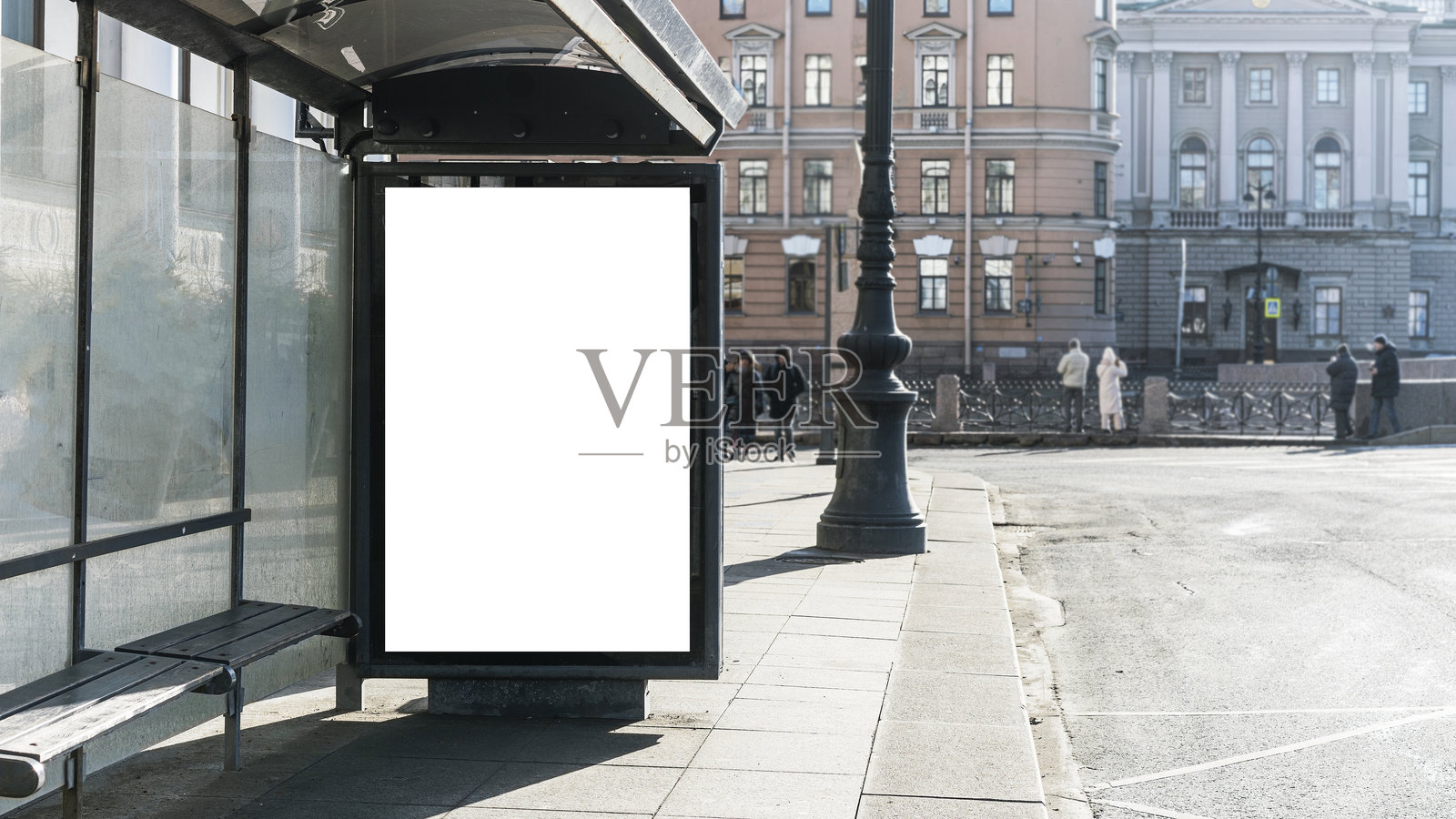 市中心公交车站的空白广告牌,背景是历史建筑和人物。公交车站设有带长凳的玻璃候车亭,区域自然采光良好照片摄影图片