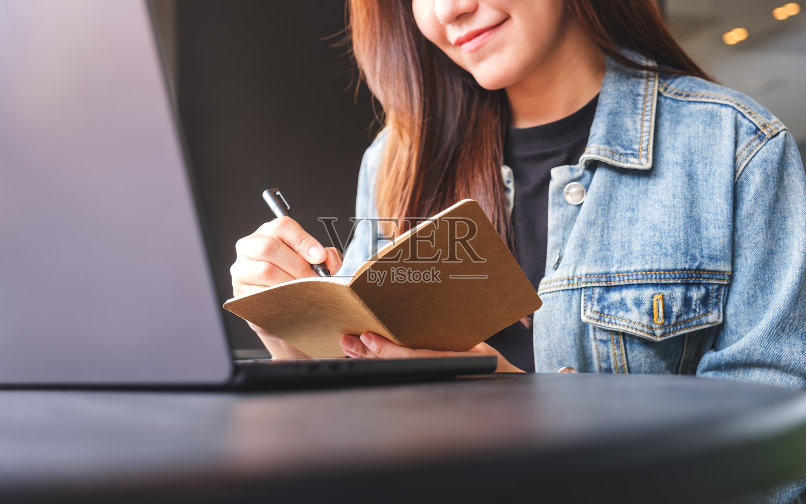 一个年轻女子在笔记本电脑上工作时在笔记本上写字的特写照片摄影图片