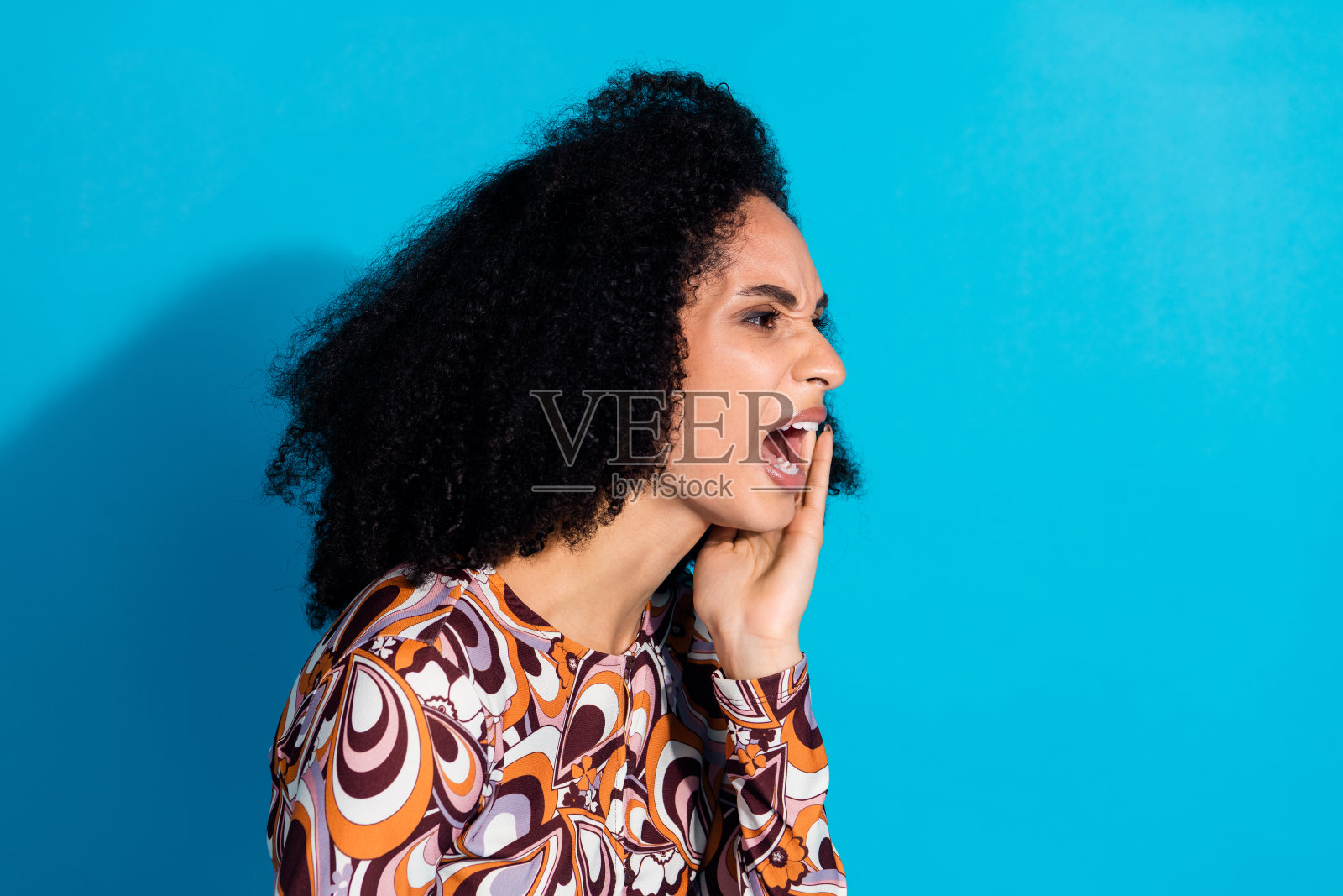 照片中疯女人穿着时髦的印花衣服,大声尖叫,空旷的空间孤立在蓝色的背景上照片摄影图片