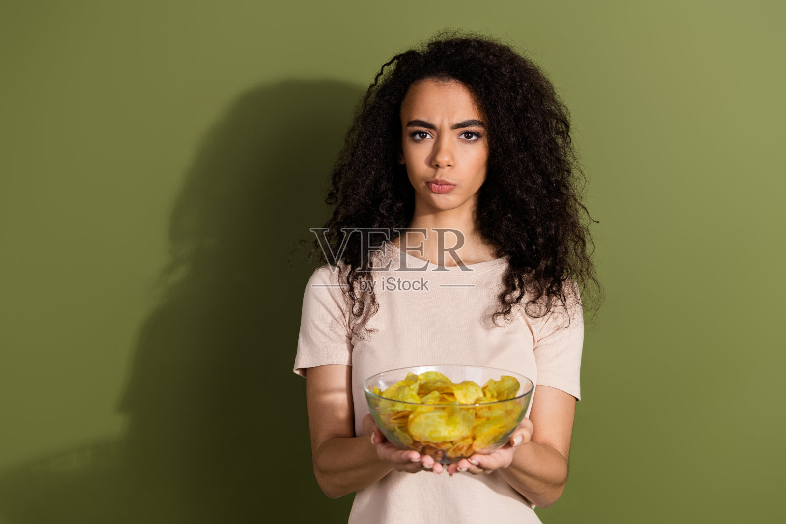 照片上困惑、忧郁、不满的女孩,波浪发型,穿着米色t恤,在卡其色背景上给你孤立的芯片照片摄影图片