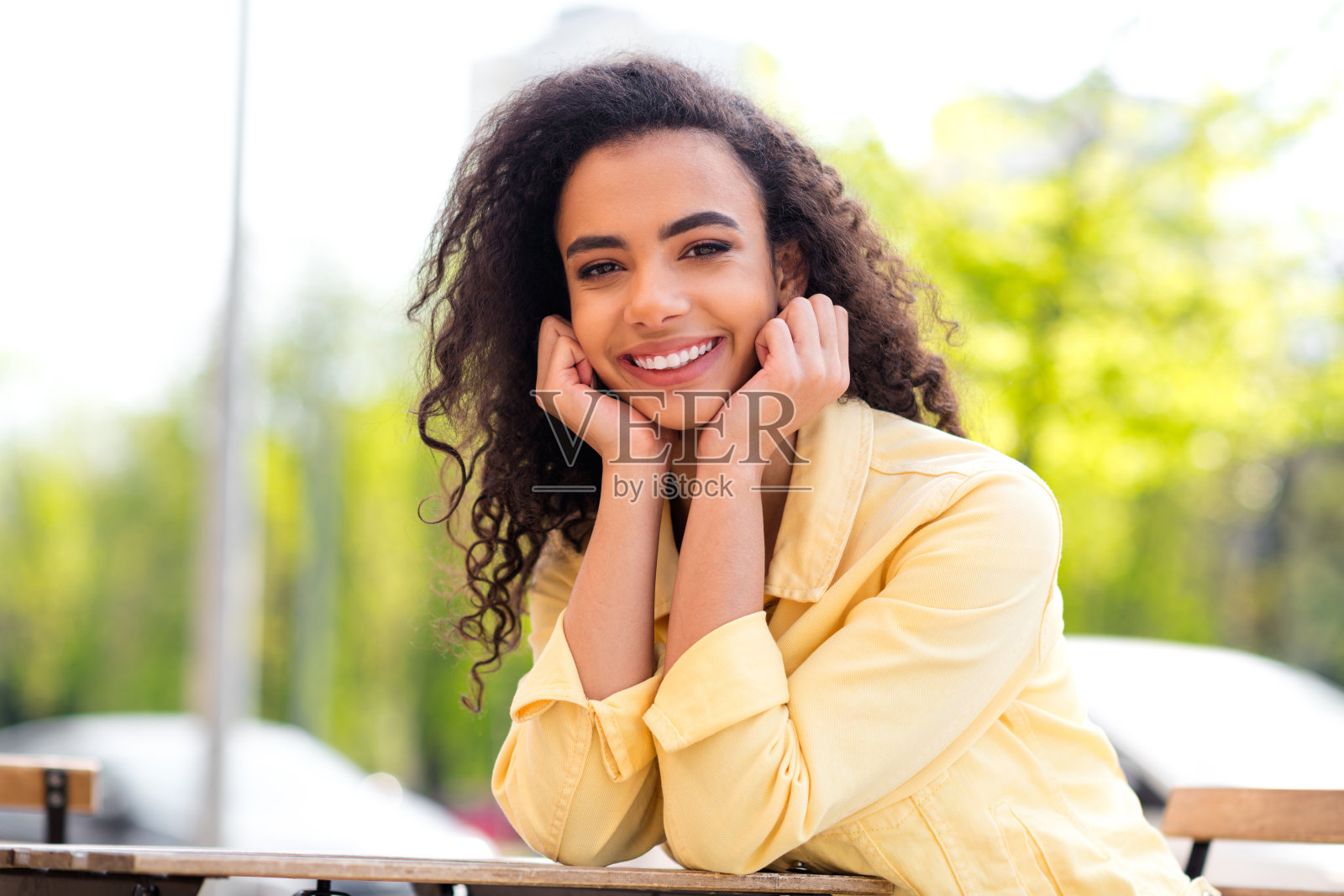 肖像积极的卷发可爱的开朗的女人梦幻坐在咖啡馆桌子穿黄色夹克散步公园阳光明媚的春天天气外面照片摄影图片