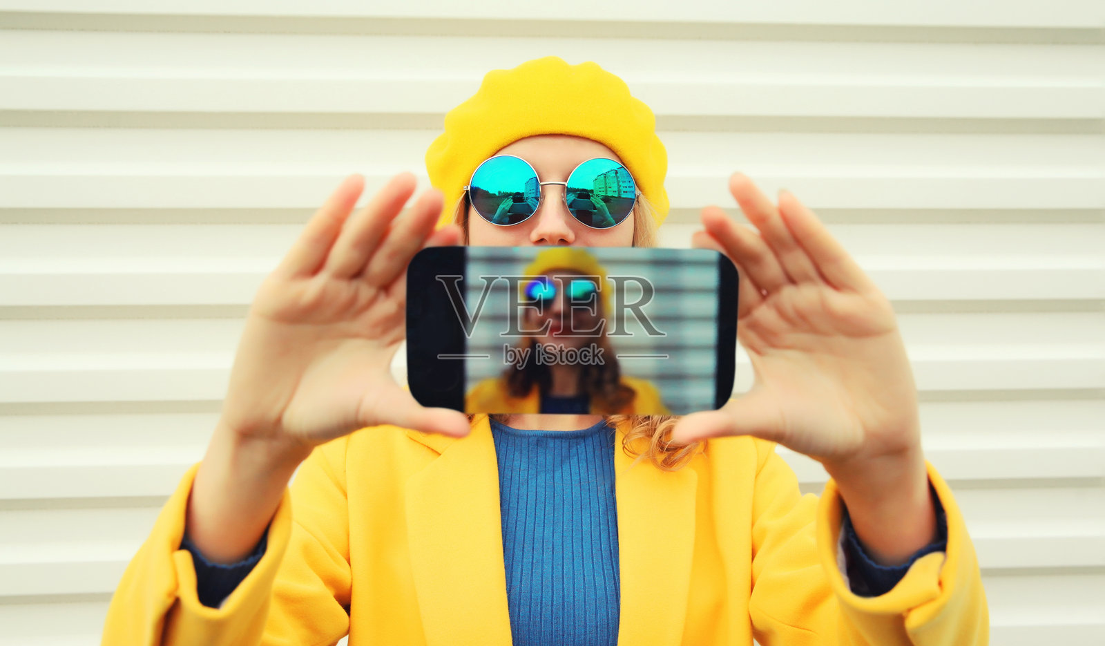 近景:现代时尚的快乐年轻女子戴着秋天黄色的法国贝雷帽,拿着手机自拍照片摄影图片