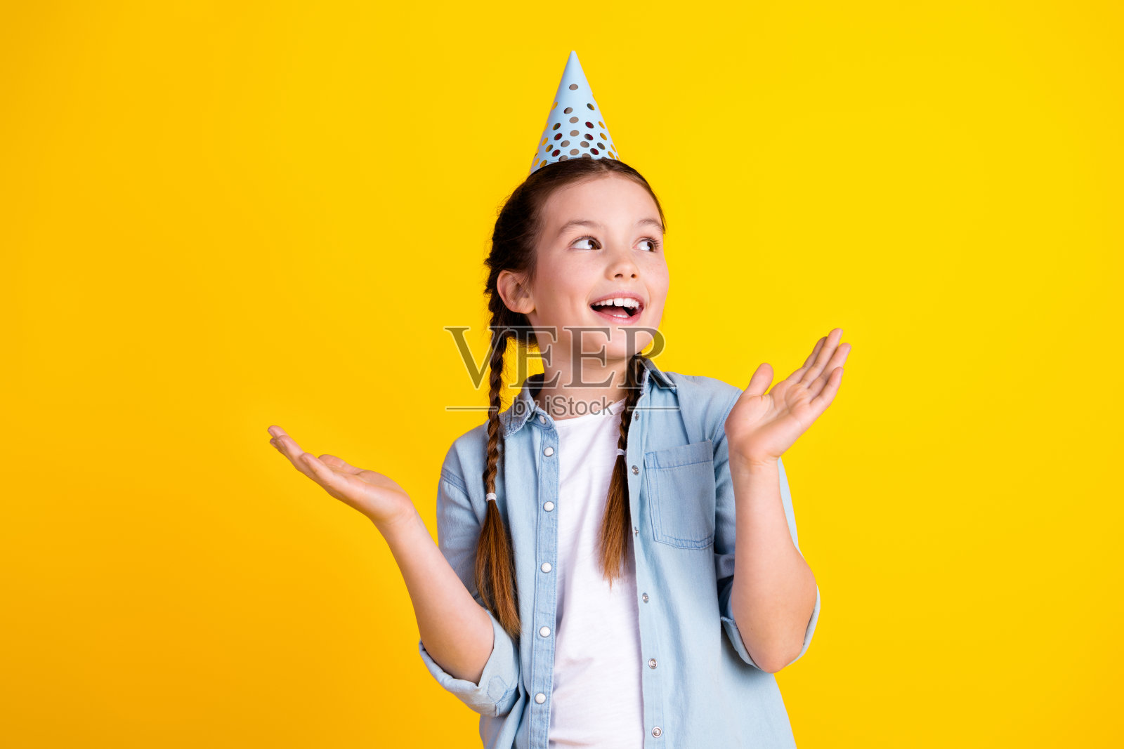 照片中迷人开朗可爱的女孩穿着时髦的牛仔服装,在黄色的背景下看起来空无一物照片摄影图片