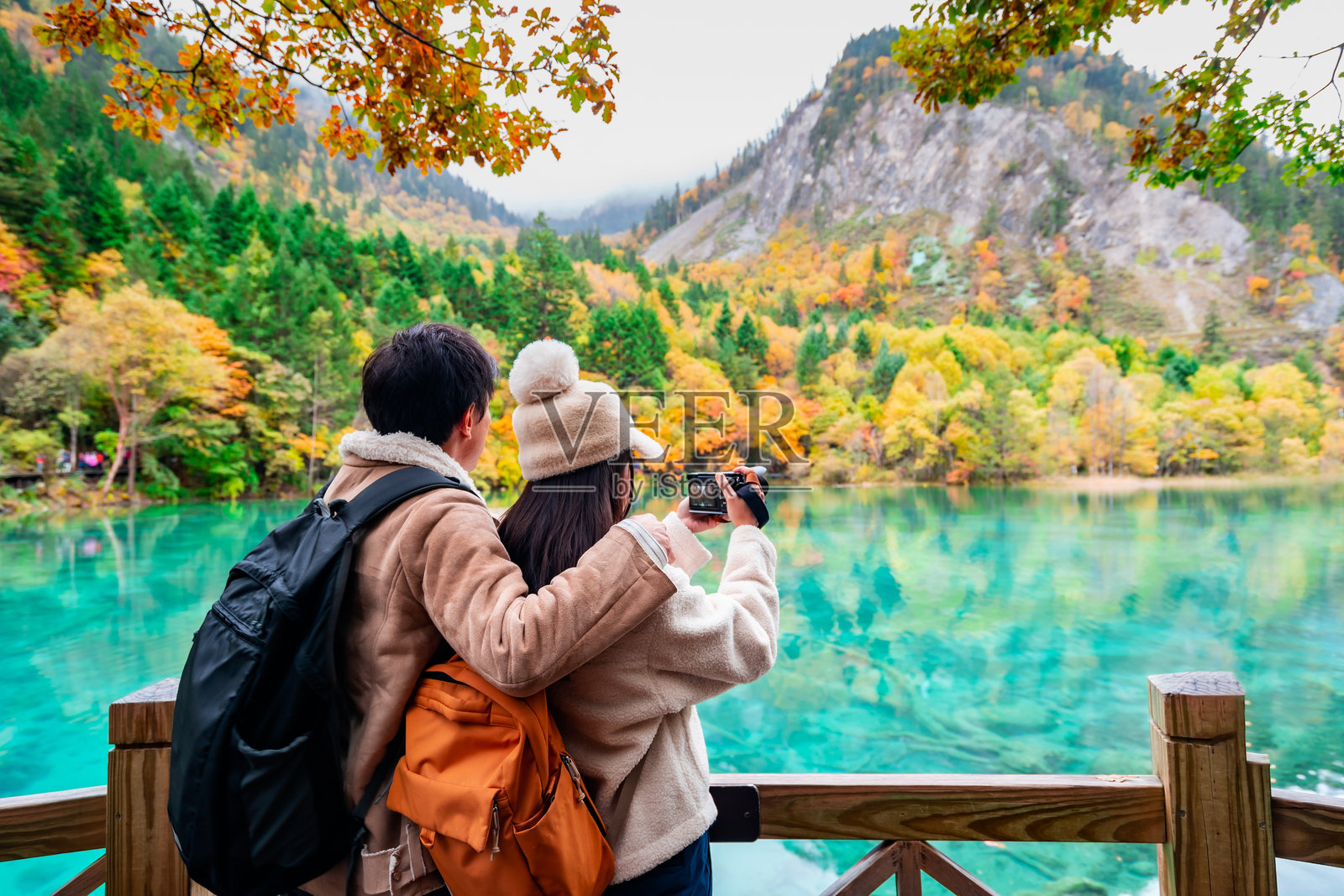 在中国成都的九寨沟国家公园里,年轻的游客夫妇正在拍摄美丽的秋景照片摄影图片
