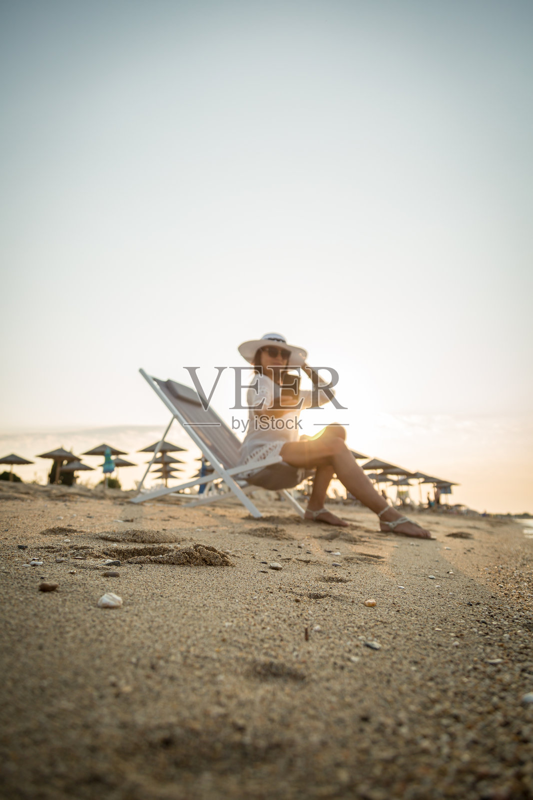 一个女人在海滩上享受着早晨的阳光和新鲜的空气,用手机刷社交媒体照片摄影图片