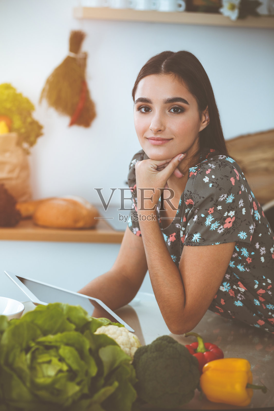在阳光明媚的厨房里,一位年轻迷人的黑发女子坐在餐桌旁,正在挑选一顿美味佳肴的食谱照片摄影图片