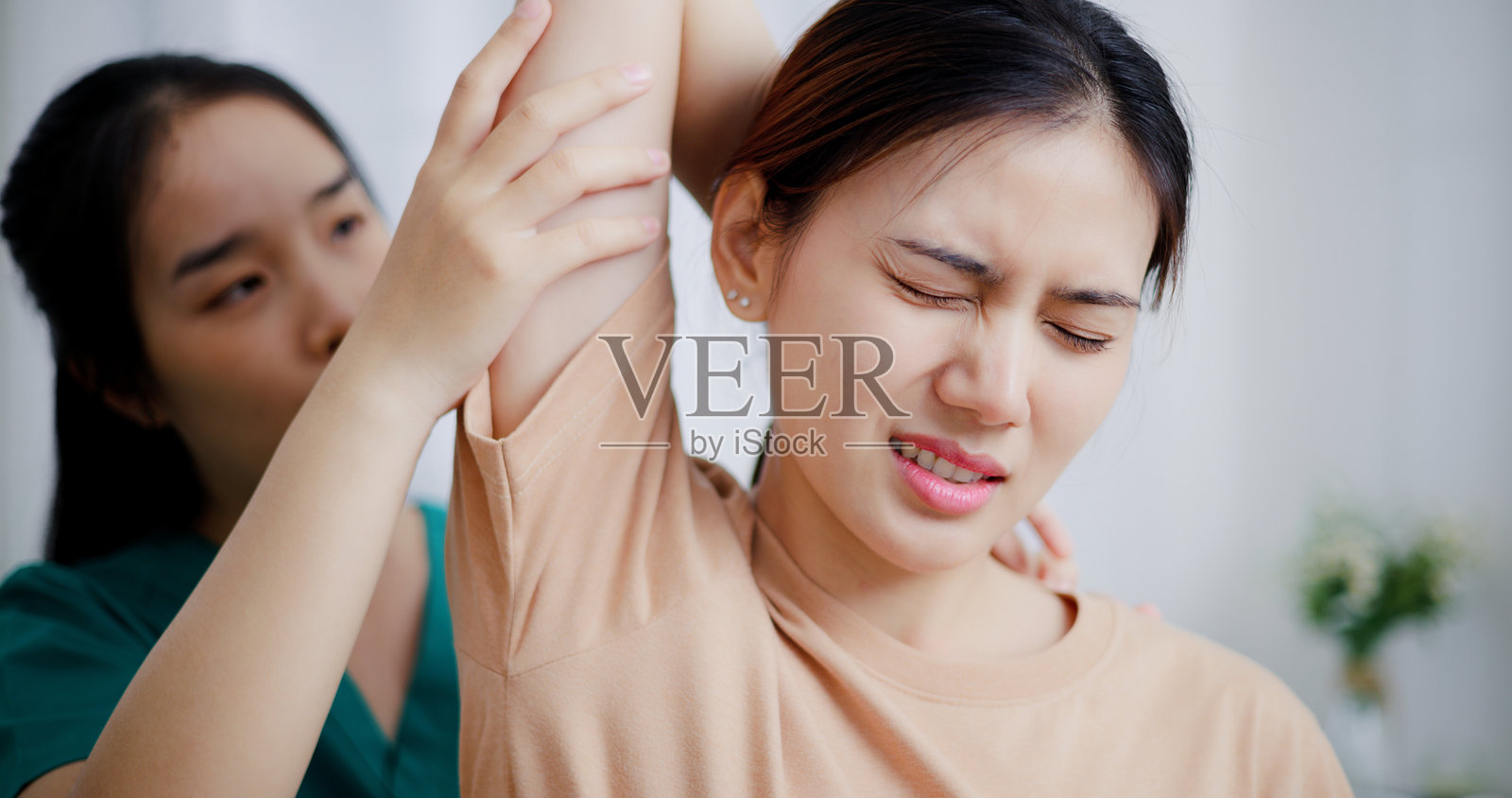 图为,在检查室里,身穿工作服的亚洲女医务人员正在为患者的手臂进行物理治疗。照片摄影图片