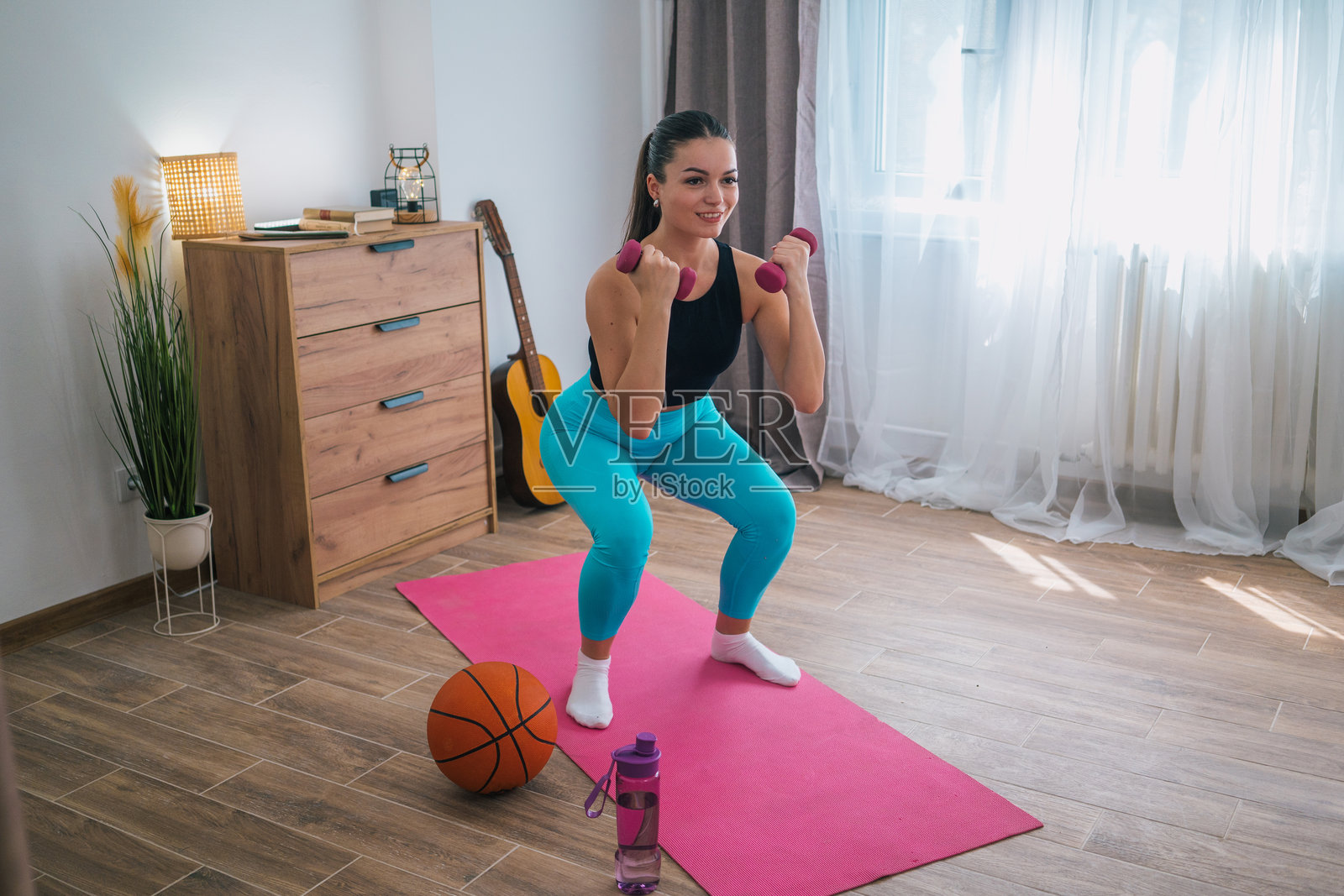 运动的年轻女子用哑铃做深蹲。在家锻炼照片摄影图片