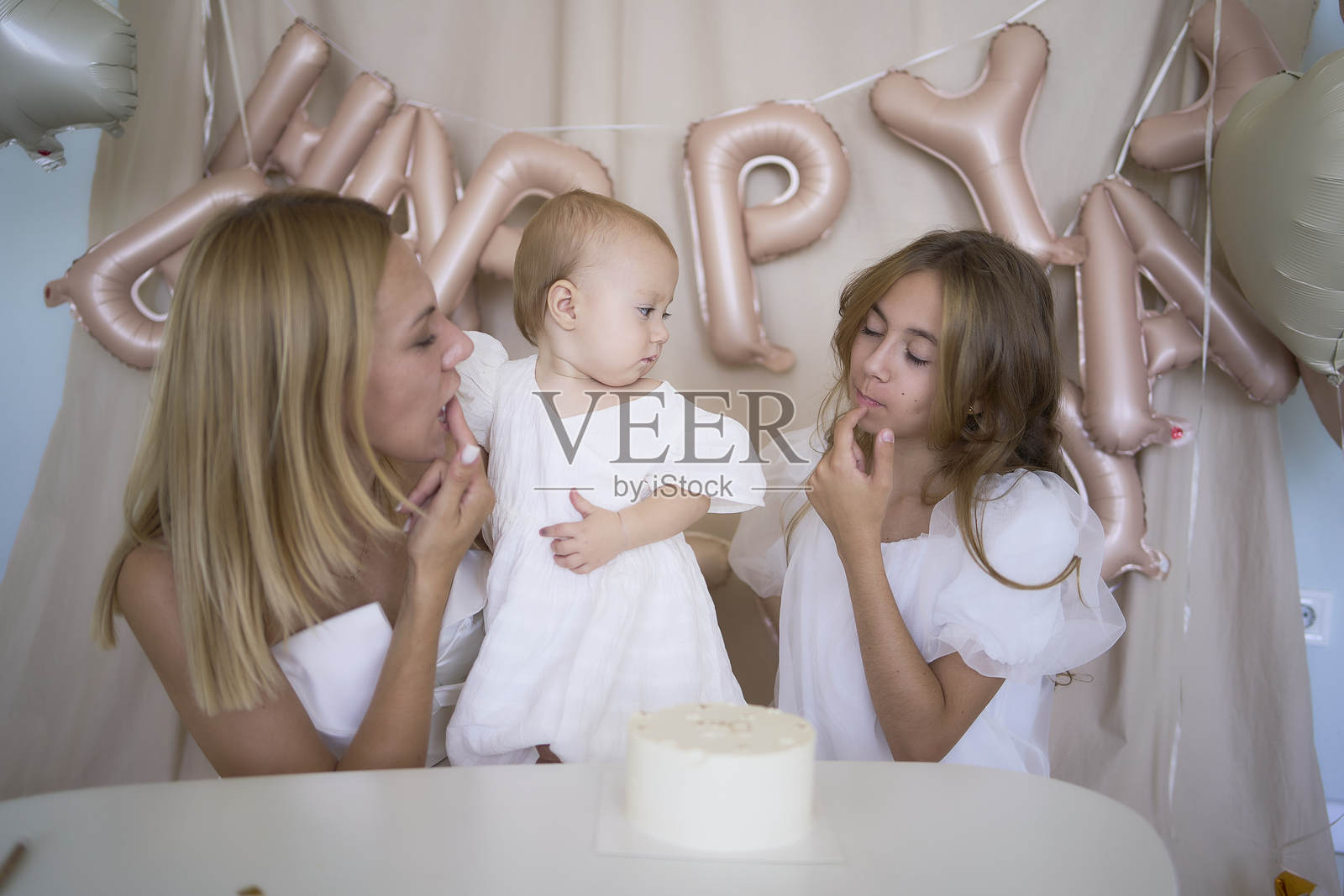 小女孩与妈妈和十几岁前的妹妹一起品尝她的第一个生日蛋糕照片摄影图片