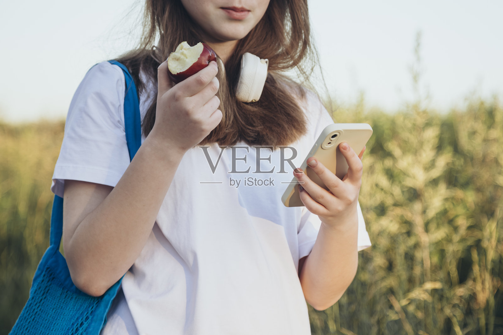 女孩正在吃苹果,看着外面的手机屏幕。照片摄影图片