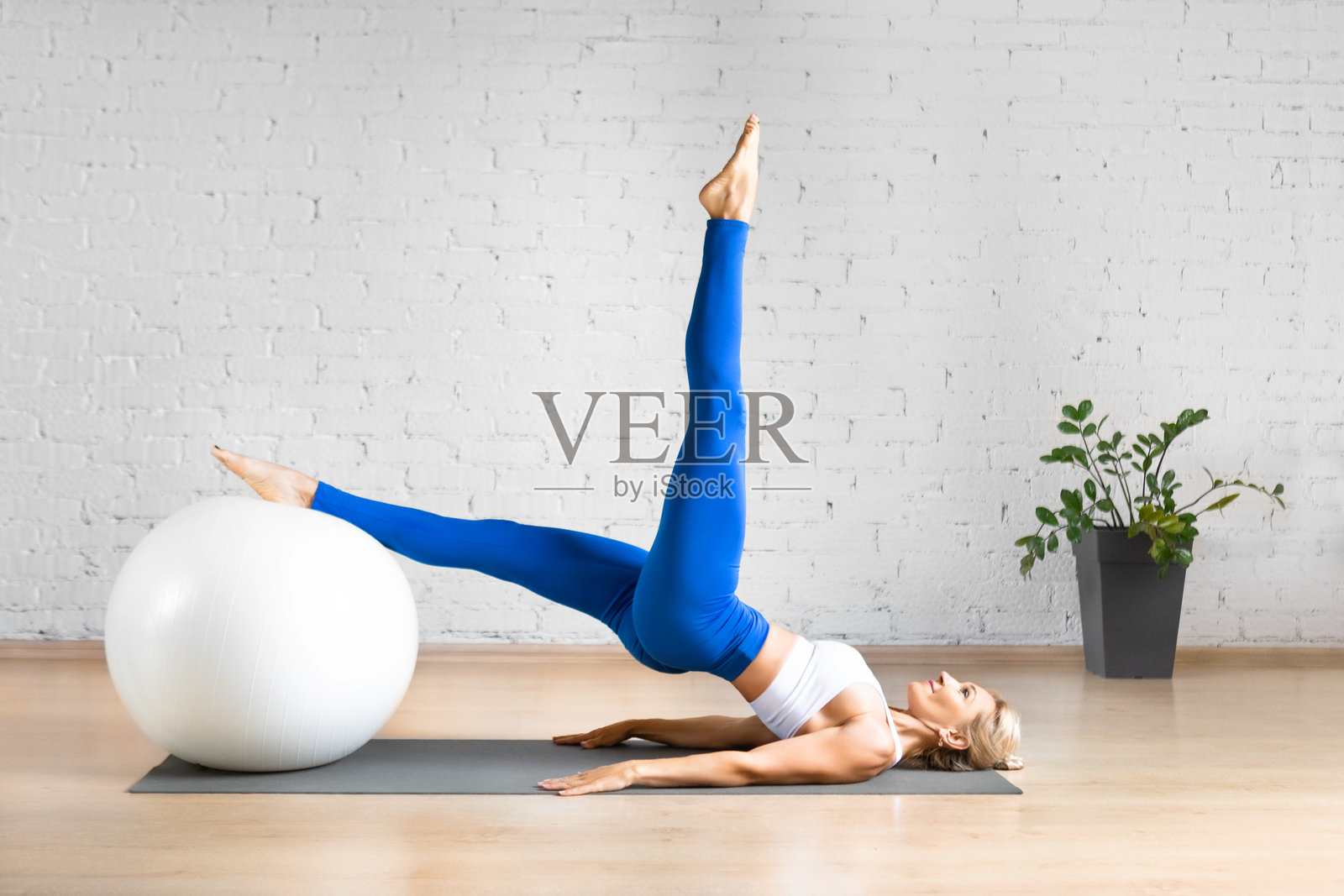 健康的白人妇女在室内阁楼工作室用健身球做单腿上的肩桥运动。照片摄影图片