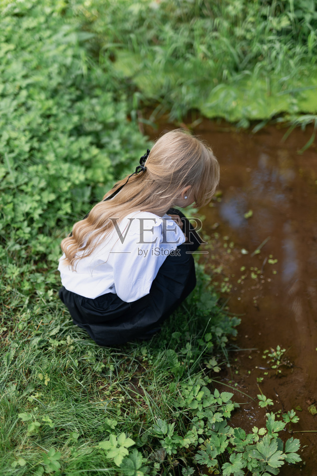一个学前班的女孩站在小溪的岸边,看着河水照片摄影图片