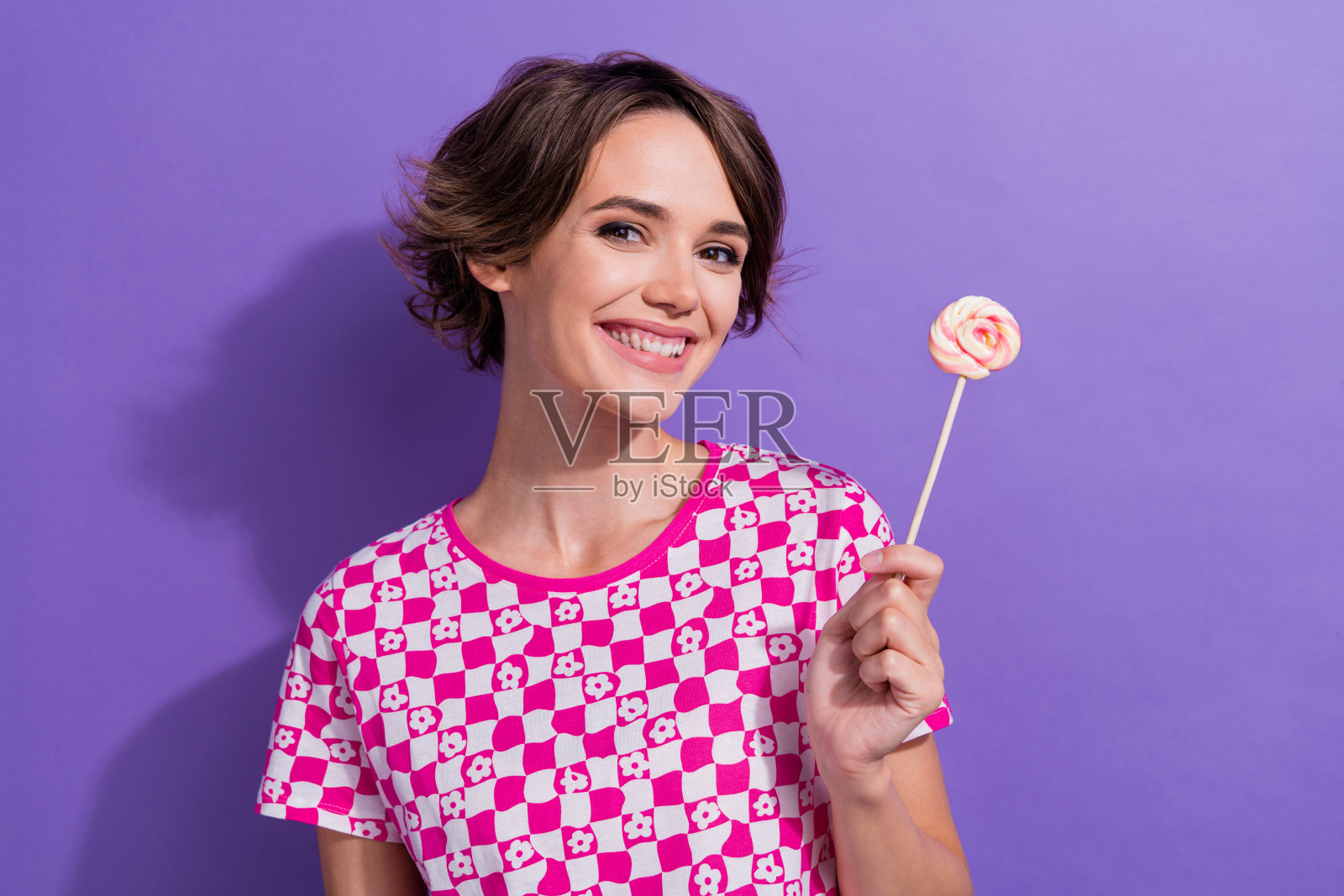 可爱甜美闪亮的女孩穿着粉红色的衣服,在紫色的背景上吃着棒棒糖照片摄影图片