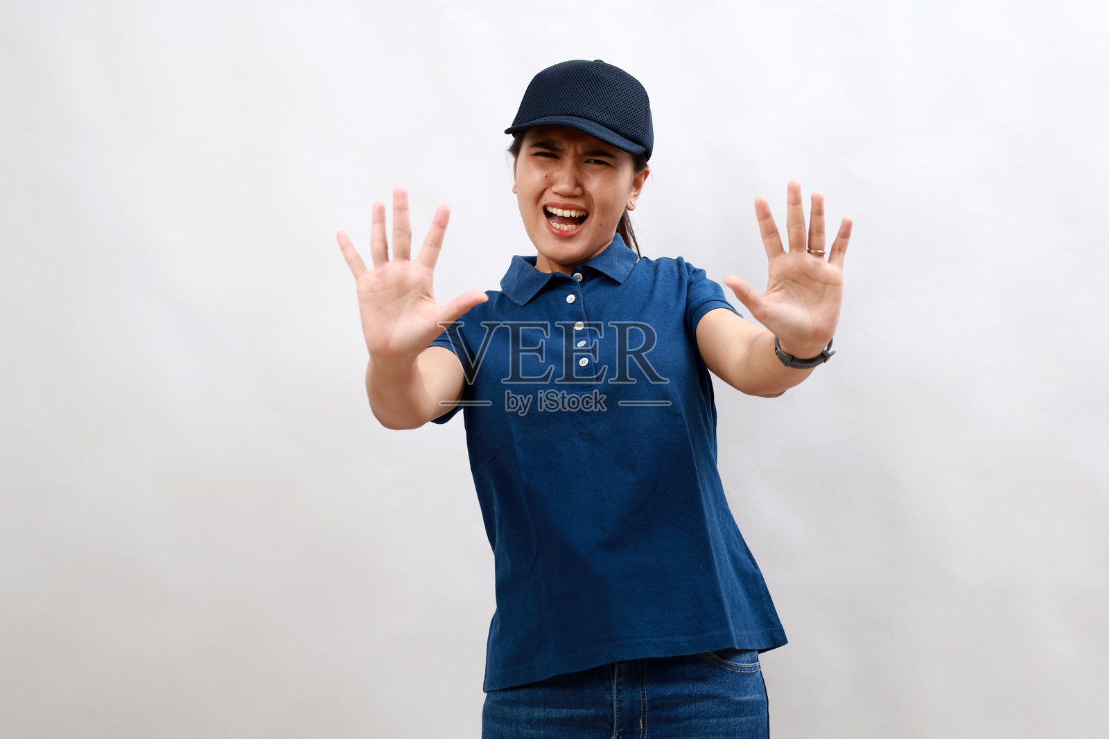 年轻的亚洲女快递员穿着快递制服,戴着帽子,害怕和害怕的表情,用手停止手势,在震惊中大喊大叫。恐慌的概念。拒绝、否认、拒绝的手势。照片摄影图片