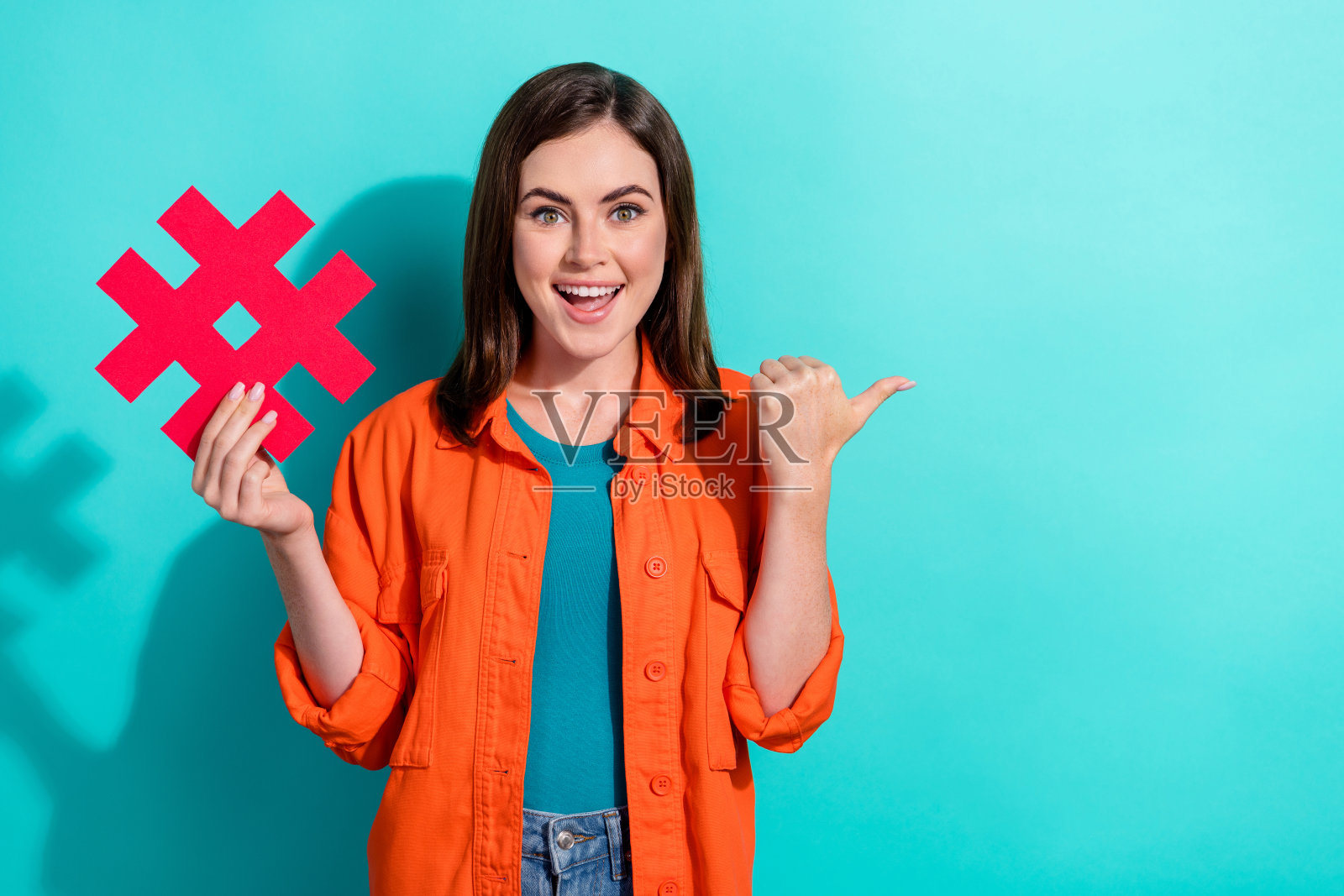喜出望外的可爱女士穿着橙色时髦的衣服,拿着纸卡,在青色背景上展示了空白的空间照片摄影图片