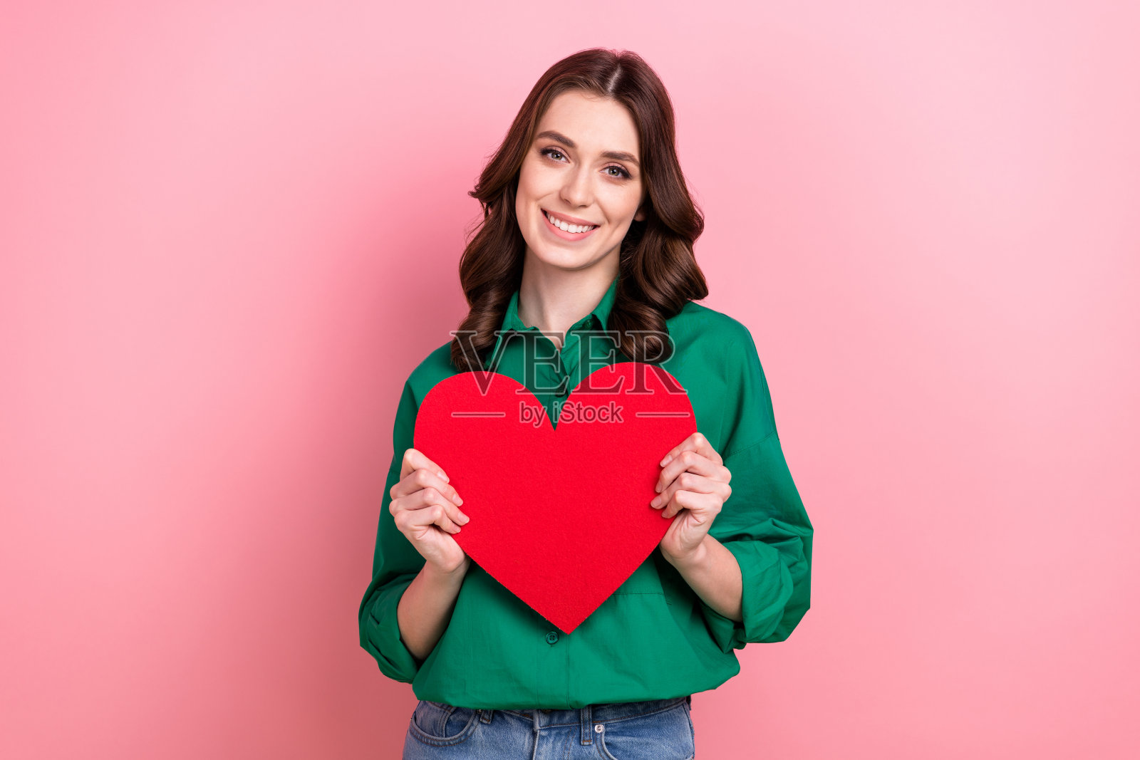 肖像积极乐观的好心情女孩卷发发型绿色衬衫持有大形状纸心孤立在粉红色的背景照片摄影图片