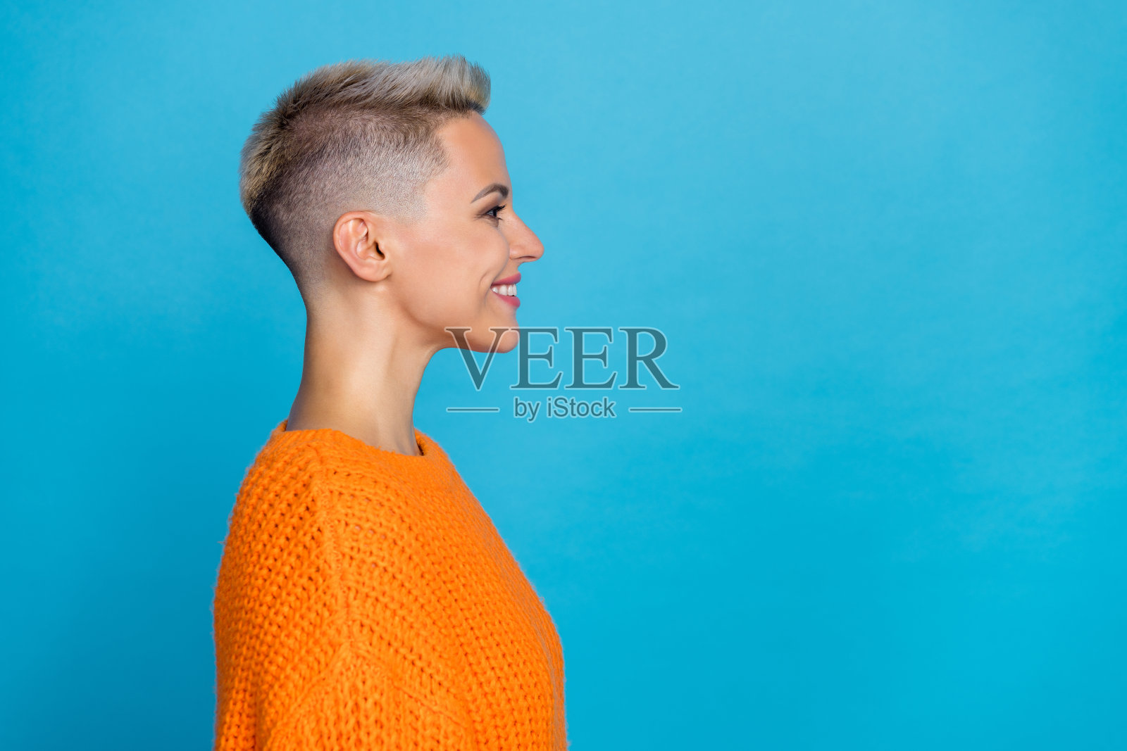 照片中可爱甜美的女子穿着针织套头衫微笑着看着空旷孤立的蓝色背景照片摄影图片