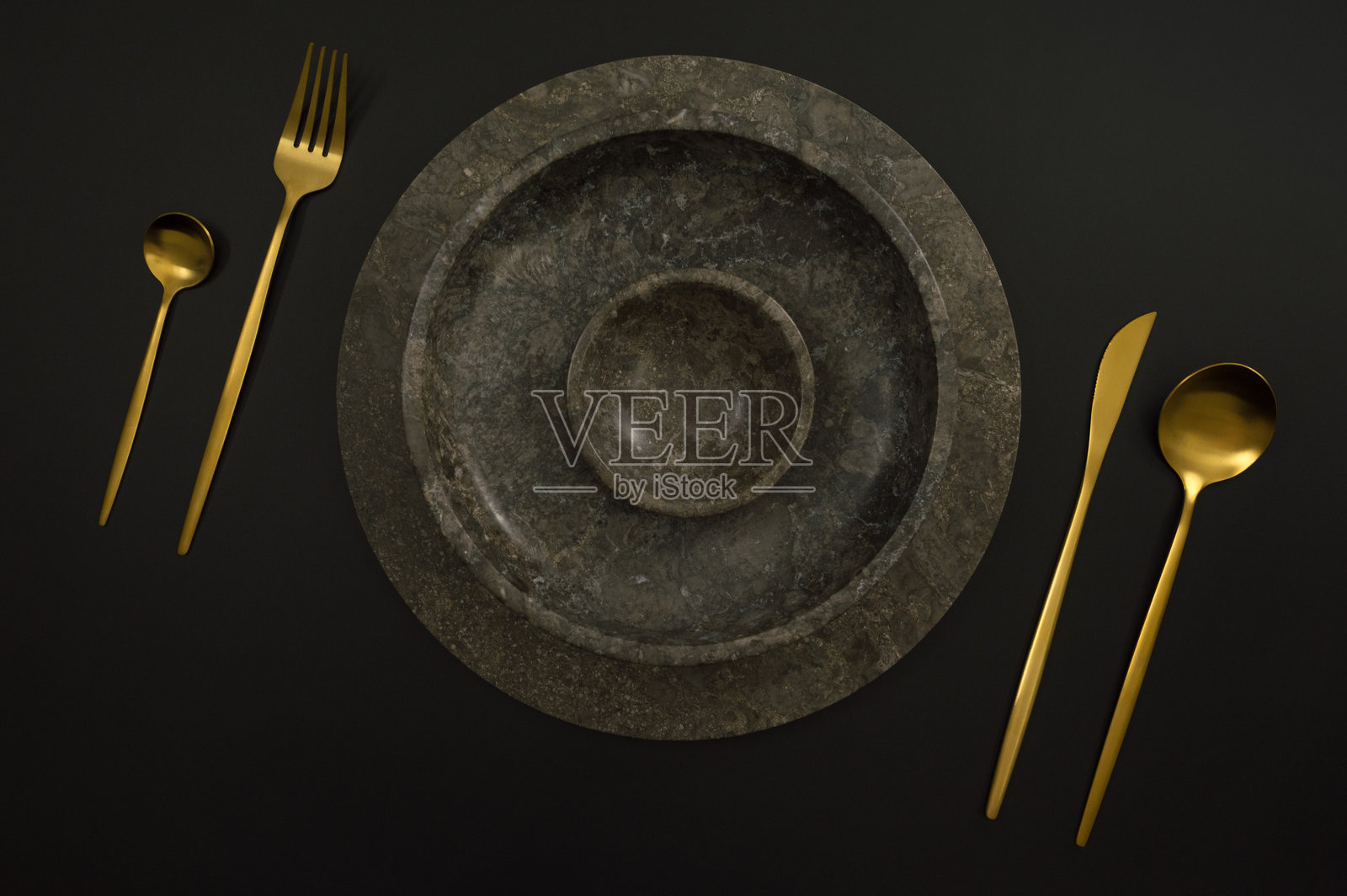 棕色大理石托盘和盘子的俯视图,黑色背景上的金色餐具。食物摆放,石盘。照片摄影图片