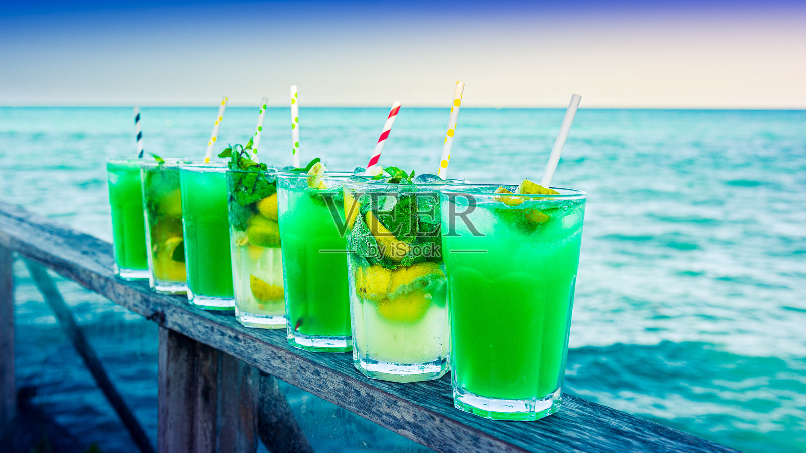 七个绿色的鸡尾酒杯对着大海排成一排照片摄影图片