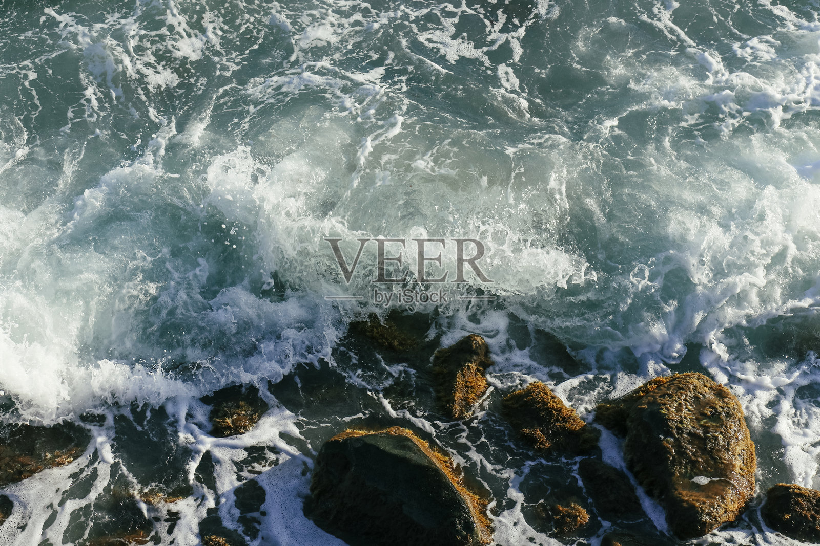 海浪拍打着覆盖着藻类的棕色岩石照片摄影图片