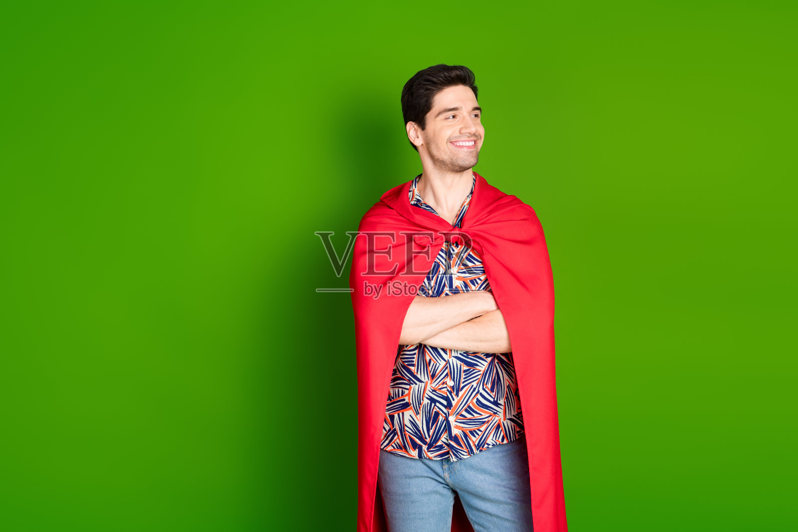 照片中自信的好男人穿着印花衬衫,红色斗篷,双臂交叉,看着销售空白空间孤立在绿色背景照片摄影图片