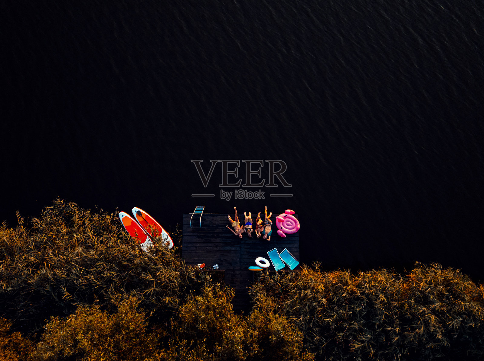 朋友们躺在湖上的码头上欣赏风景朋友们躺在湖上的码头上一边喝着啤酒一边享受夏日。边喝啤酒边迎夏日。照片摄影图片