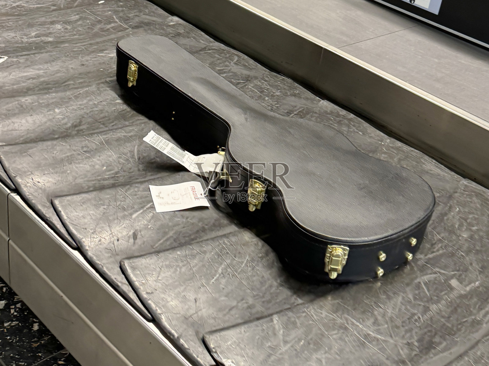 机场单层行李传送带上的黑色吉他箱,行李认领传送带,保护箱中的乐器的特写图像,重点放在前景,高架视图,旅行概念照片摄影图片