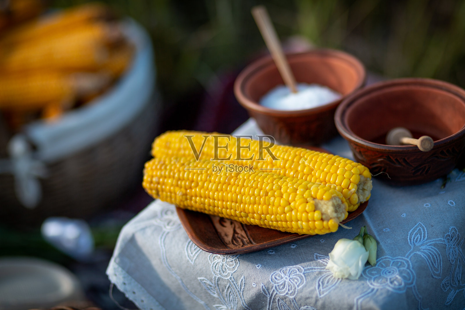 两个煮熟的玉米穗,背景是两个盛有盐和蜂蜜的粘土碗照片摄影图片