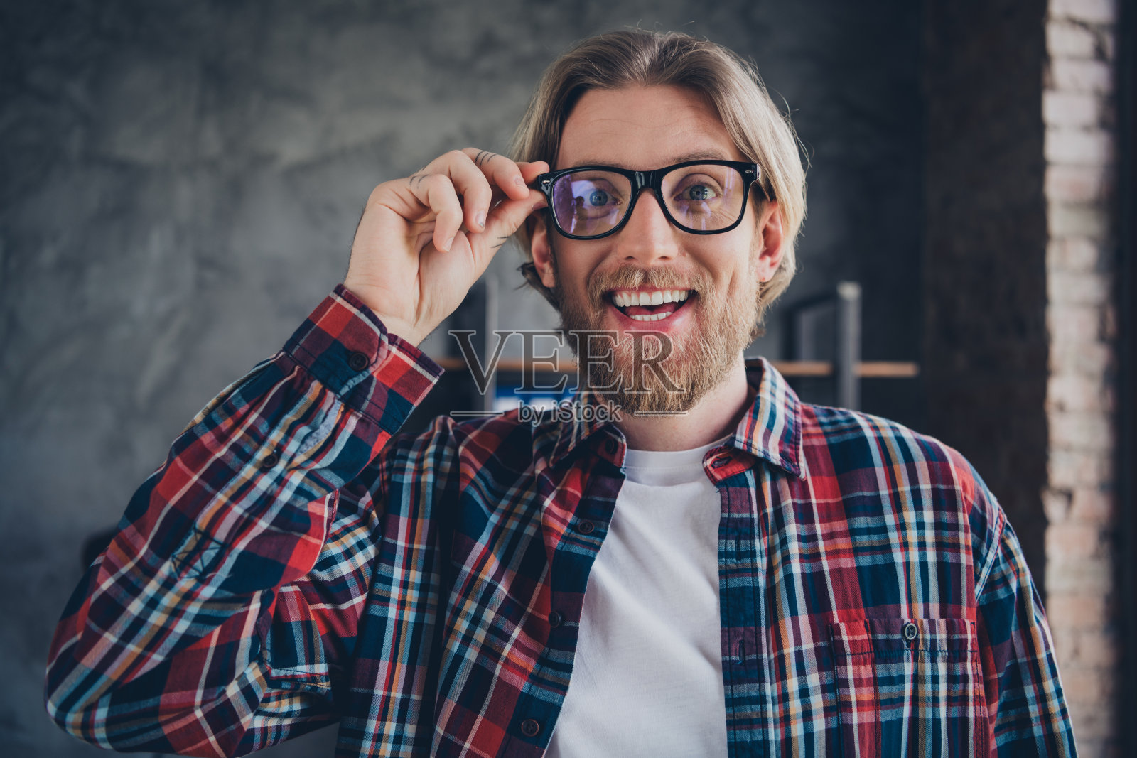 照片漂亮的年轻男性兴奋触摸眼镜穿格子衬衫舒适的现代办公室阁楼房间室内室内商人的工作空间照片摄影图片