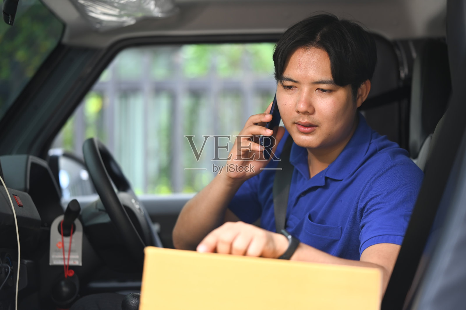 年轻的快递员坐在一辆面包车里打电话。运输和交付服务的概念照片摄影图片