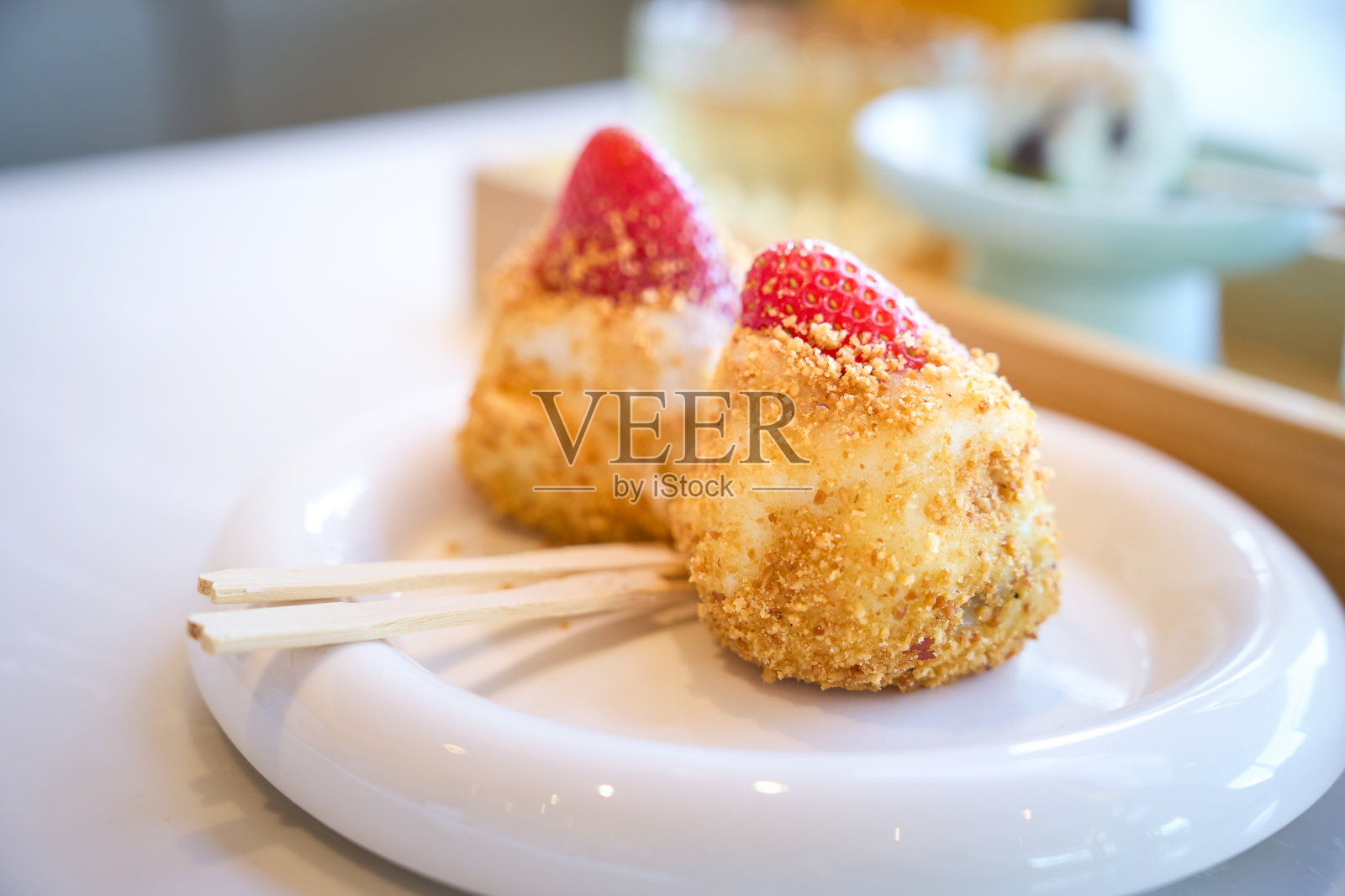 白色的盘子里放着两片涂着草莓的大福麻糬照片摄影图片