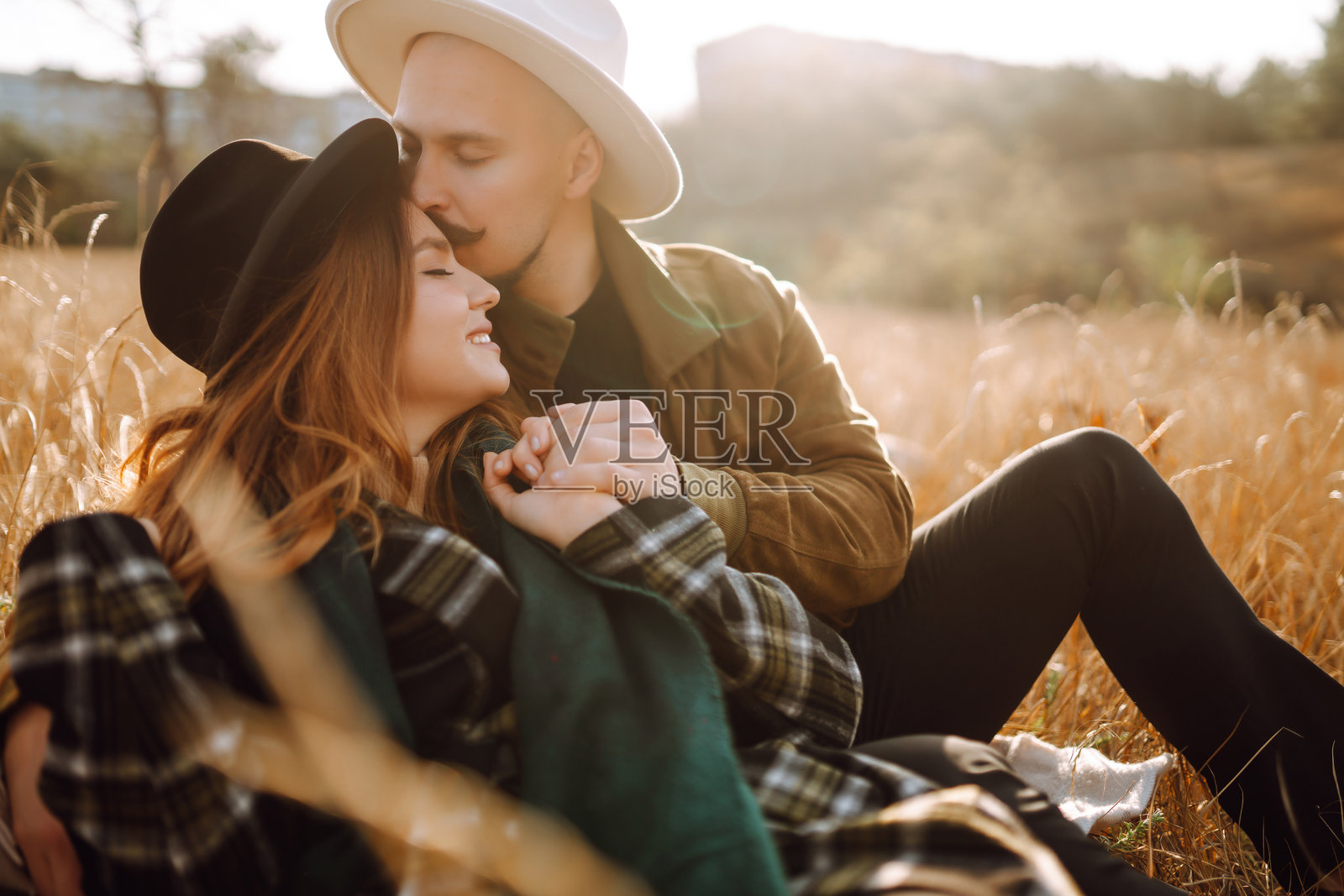 在一个温暖的秋日午后,一对夫妇坐在山间的田野里拥抱在金色的阳光下。照片摄影图片