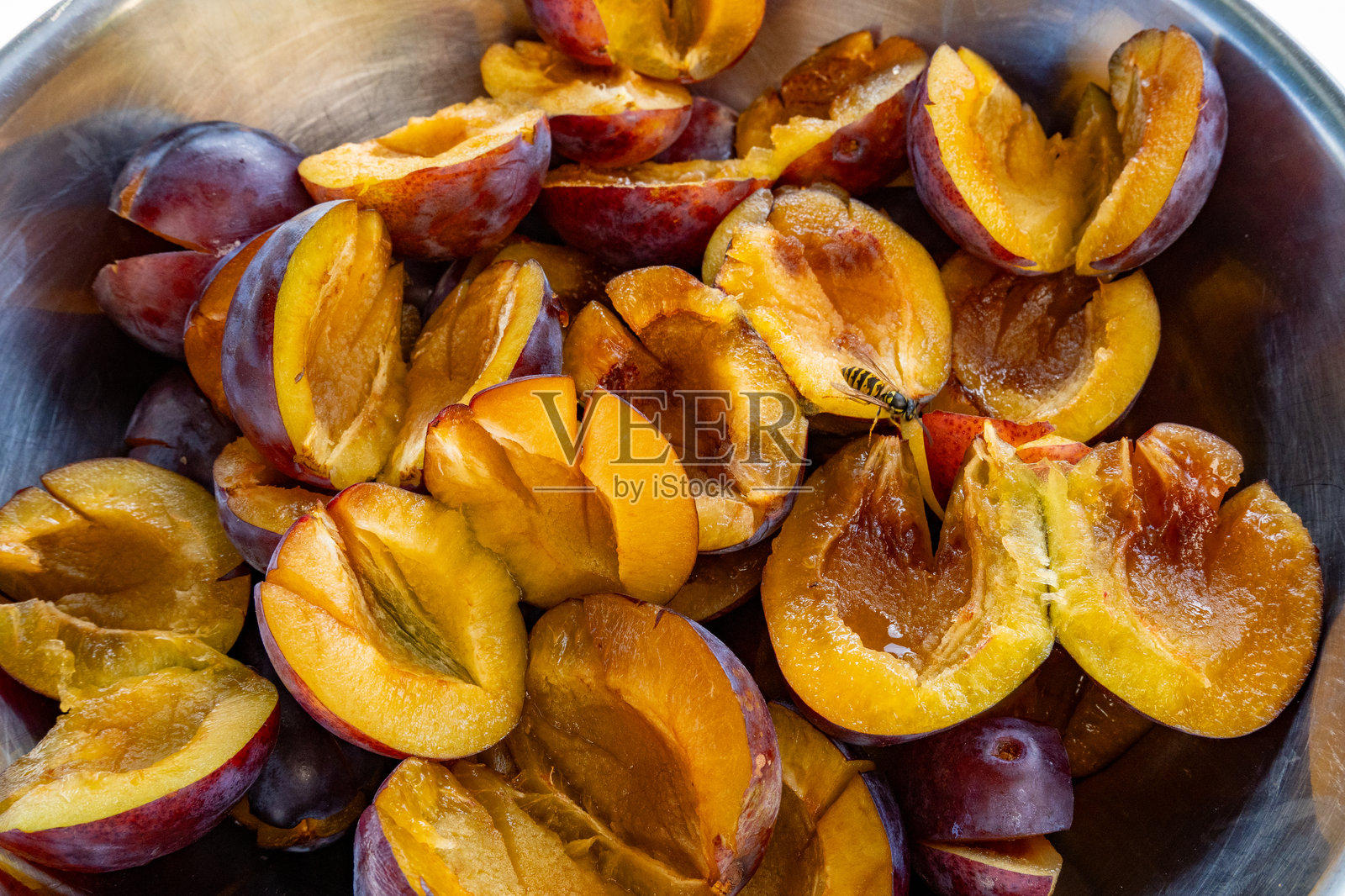 去核梅子(Prunus domestica亚科)。在一个银碗里。一只黄蜂正在啃食香甜的果实照片摄影图片