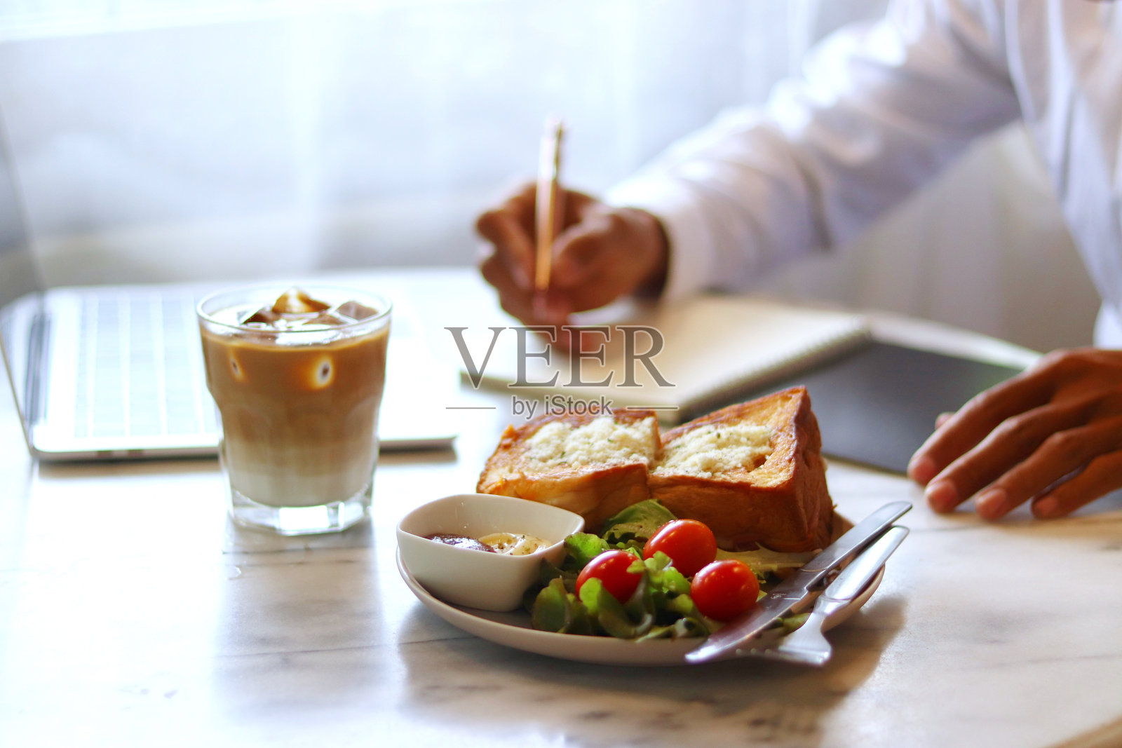 早餐摆放在一个男人的桌子上,他正坐着工作,一边吃早餐,一边端着一杯摆放精美的咖啡。照片摄影图片