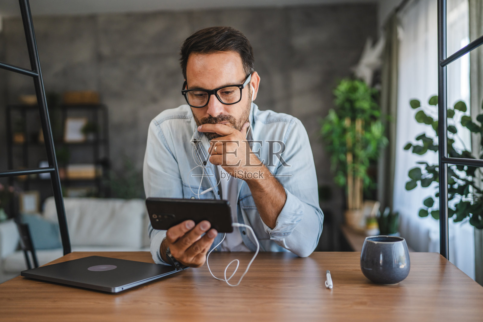 戴眼镜的成年男子在家庭办公桌旁使用手机照片摄影图片