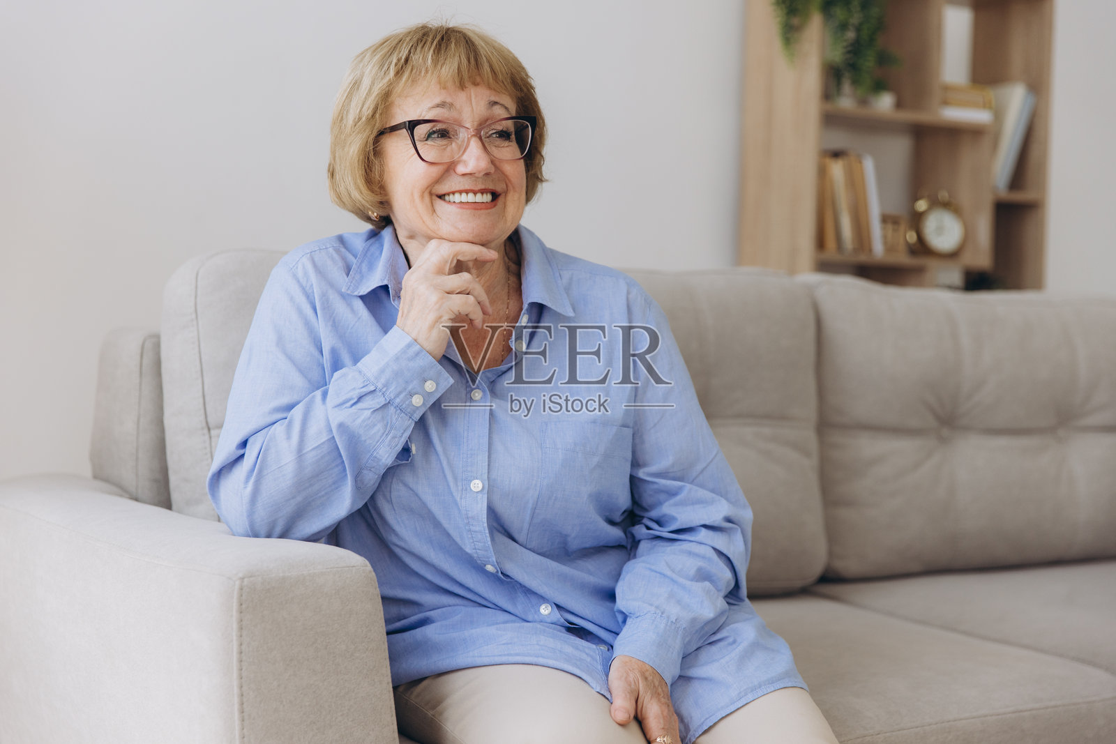 面带微笑的老年金发女子看着镜头,快乐的老太太戴着眼镜在家里室内摆姿势,积极的单身老年退休女性坐在客厅沙发上的大头照照片摄影图片