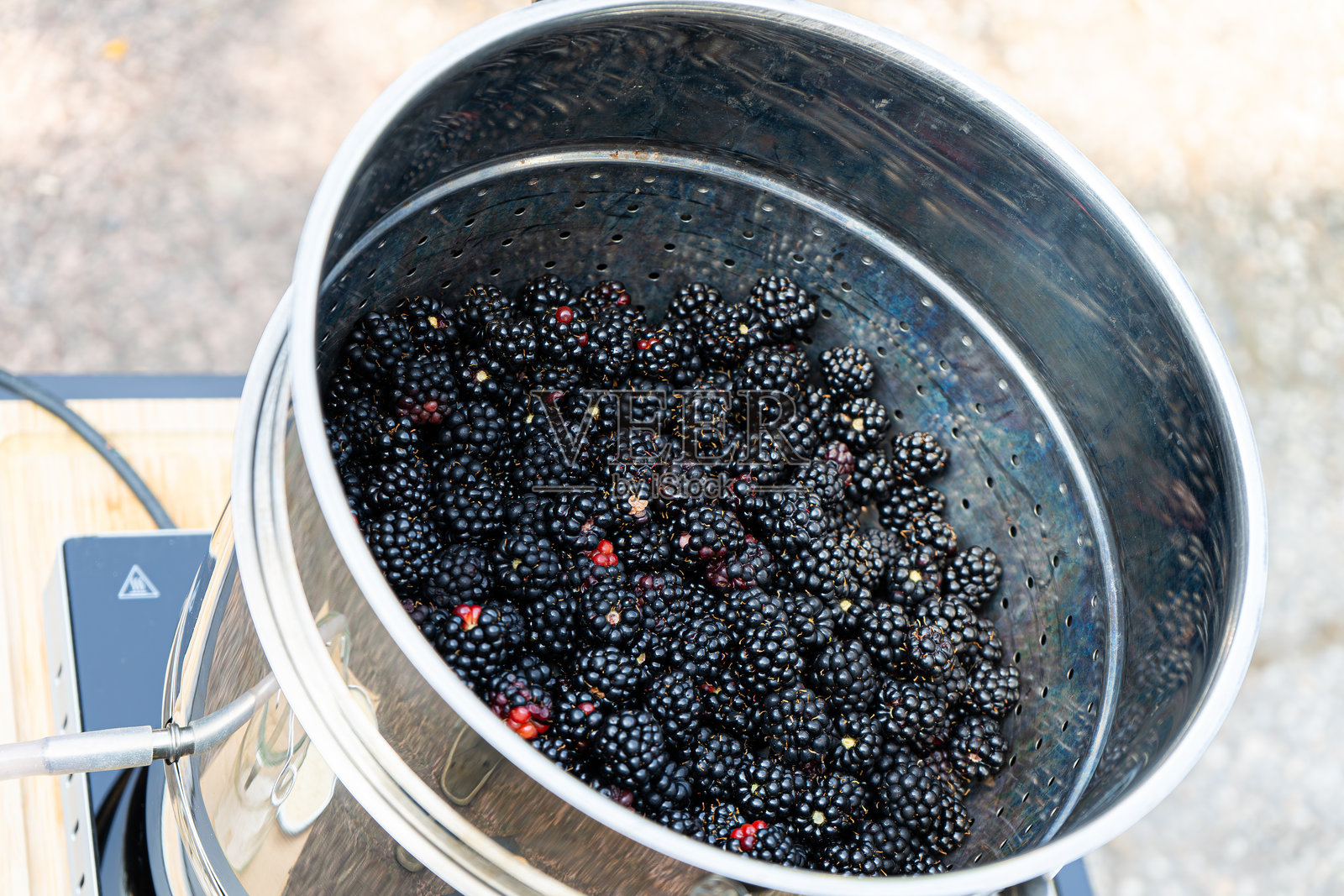 用蒸汽榨汁机制作黑莓汁。自制花园黑莓在蒸汽榨汁机做出深红色的果汁。制作甜的深红色黑莓汁。照片摄影图片