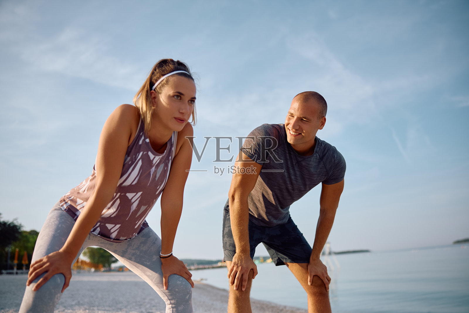 年轻的运动员夫妇在海滩上跑步后休息。照片摄影图片