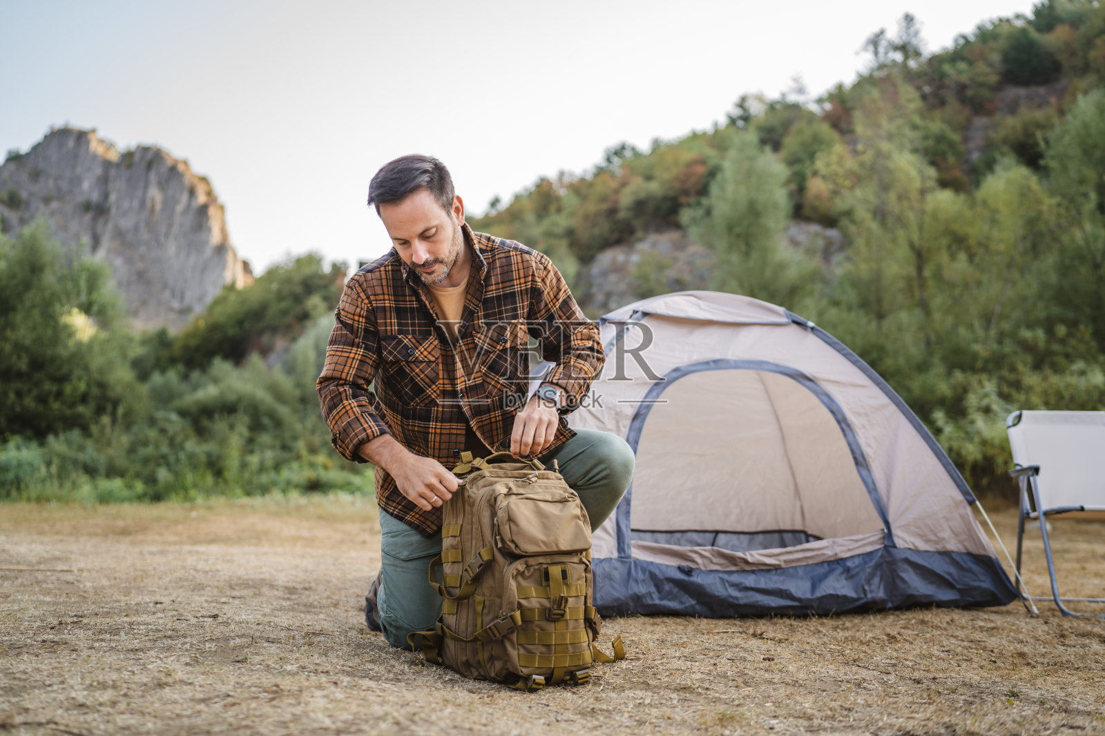 一名成年男子跪在地上收拾背包,准备露营后回家照片摄影图片