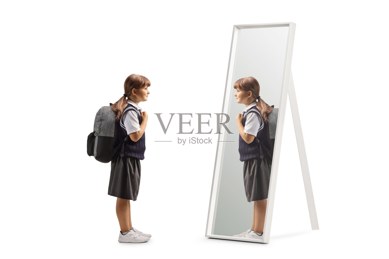 穿着校服的女孩站在那里,肩上背着背包,看着镜子照片摄影图片