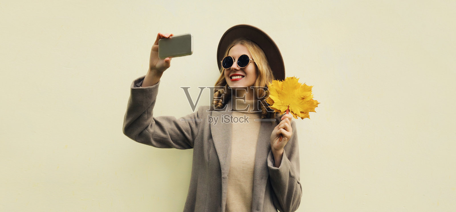 秋天,时尚快乐的年轻女子拿着手机自拍,手里拿着黄叶照片摄影图片