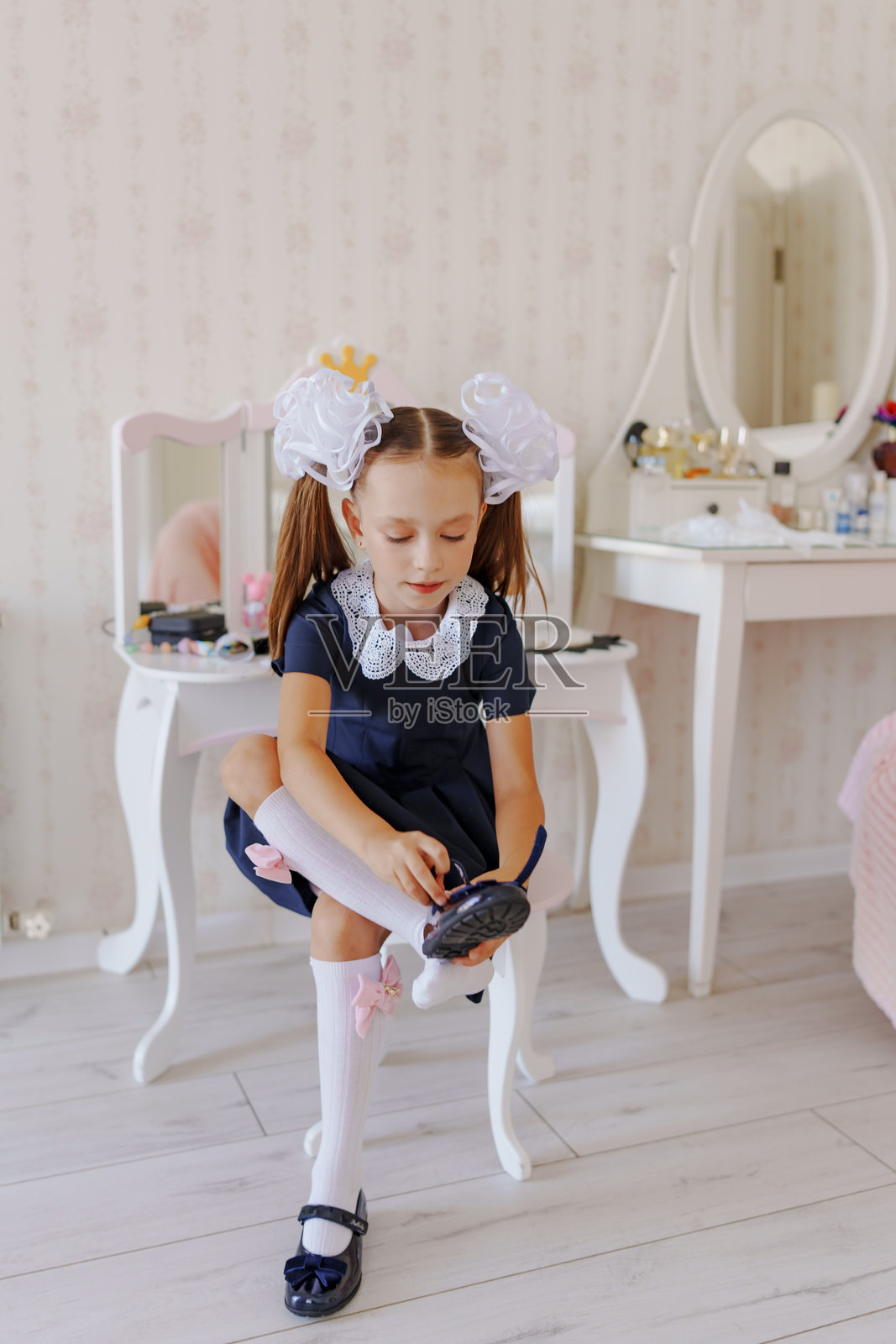 一个穿着校服的小女孩在梳妆台上穿鞋。照片摄影图片