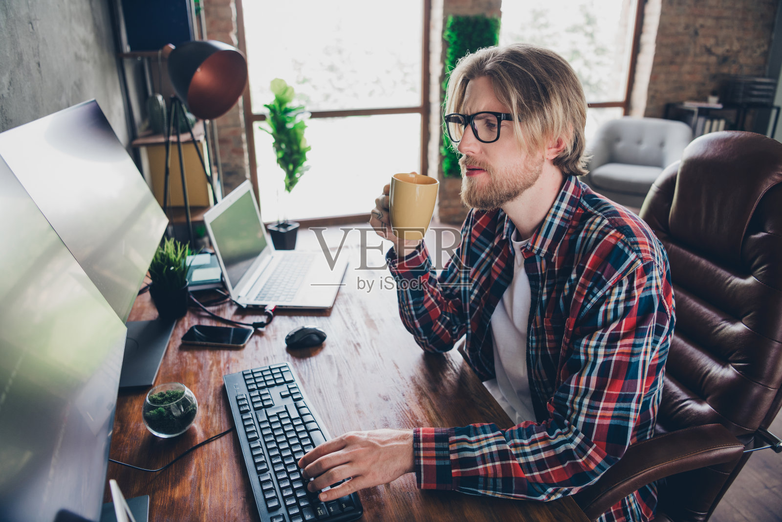 年轻的高级it专家程序员男子的照片,金发碧眼,戴着眼镜,穿着格子衬衫,坐在工作场所喝咖啡照片摄影图片