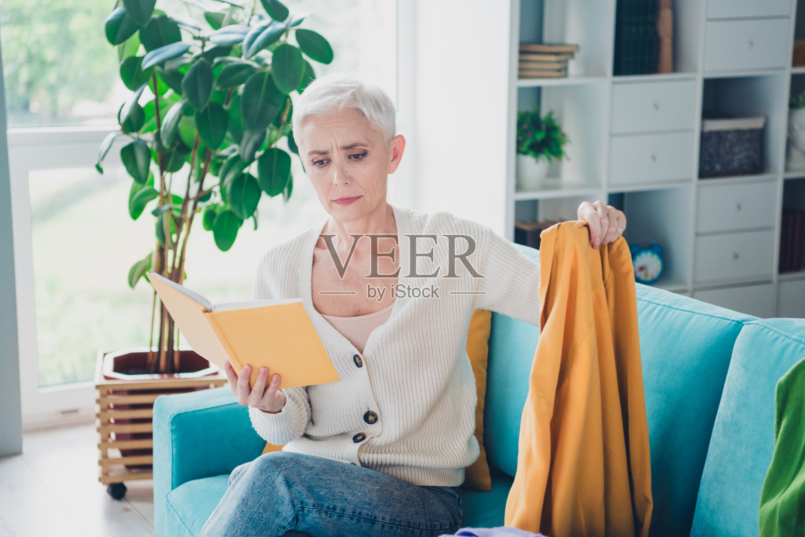 照片迷人可爱的老年妇女穿着白色开襟羊毛衫抱规划师脏套头衫读家里打扫室内的任务照片摄影图片