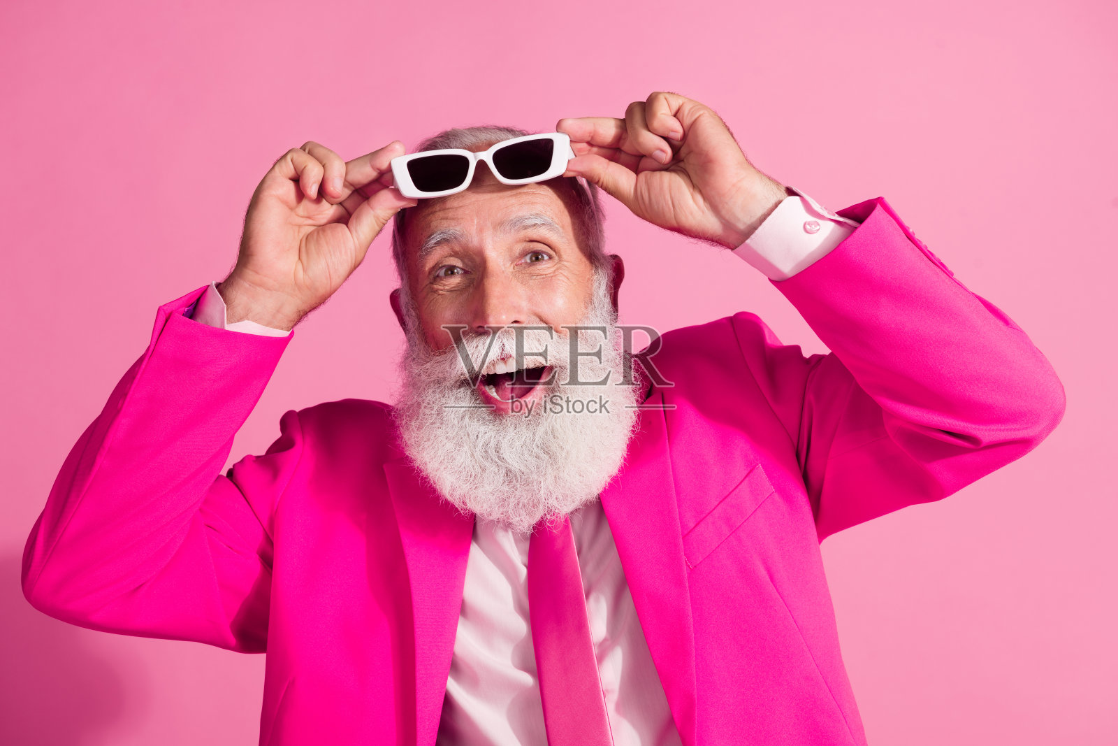 迷人的白发老人的照片圣诞老人mc演出者脱下太阳镜,穿着时尚的粉红色西装孤立在柔和的颜色背景照片摄影图片