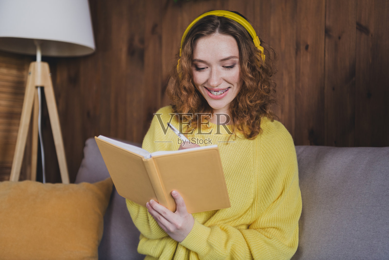 照片迷人的年轻女性写笔记本耳机穿着黄色毛衣舒适的日光家室内客厅照片摄影图片