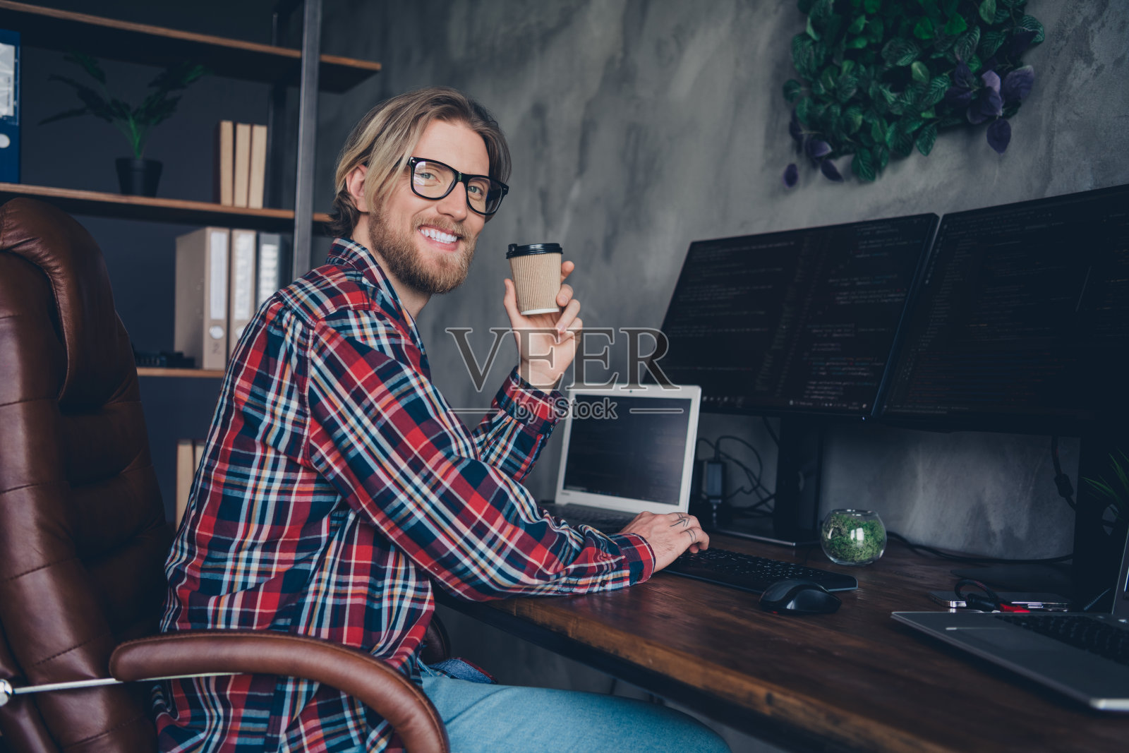 金发年轻商人自己创业数据科学的照片坐在老板扶手椅工作站和电脑在办公室喝咖啡照片摄影图片