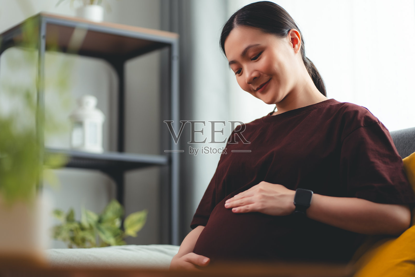 亚洲孕妇喜欢坐在家里客厅的沙发上放松。照片摄影图片